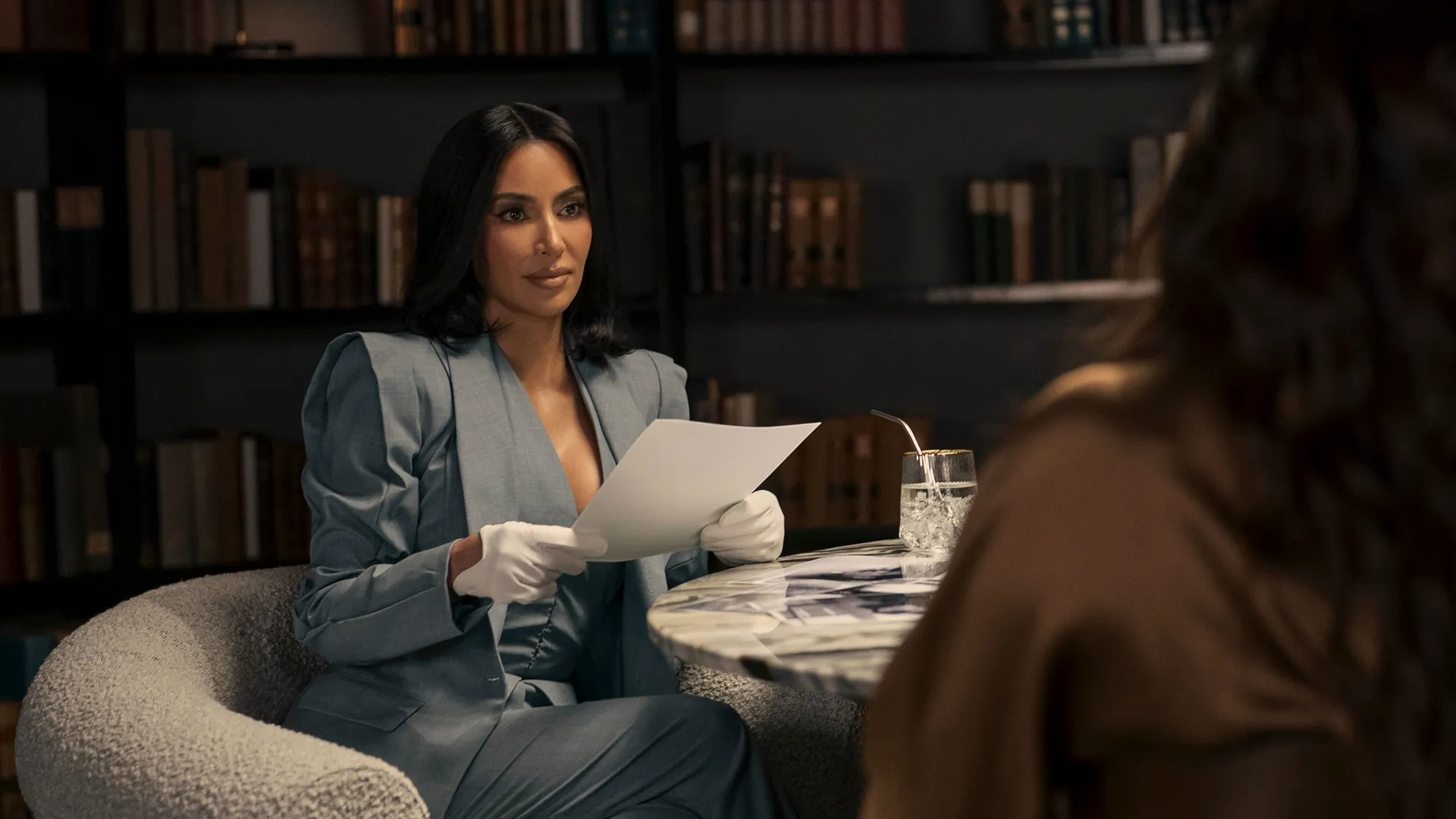 Kim Kardashian as Allura Grant in All's Fair sitting at a tale with another woman holding legal documents.