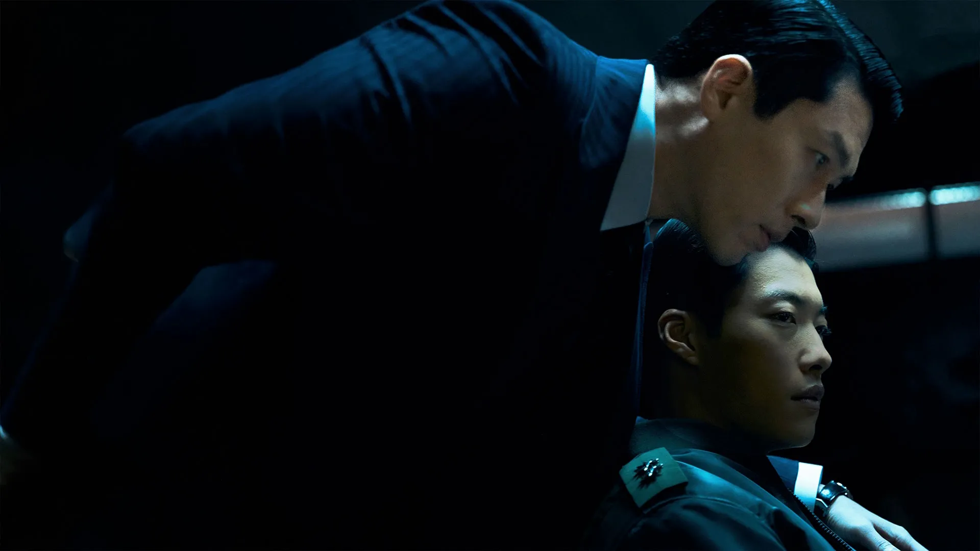 Two people in formal clothing sit closely together in a dimly lit room.