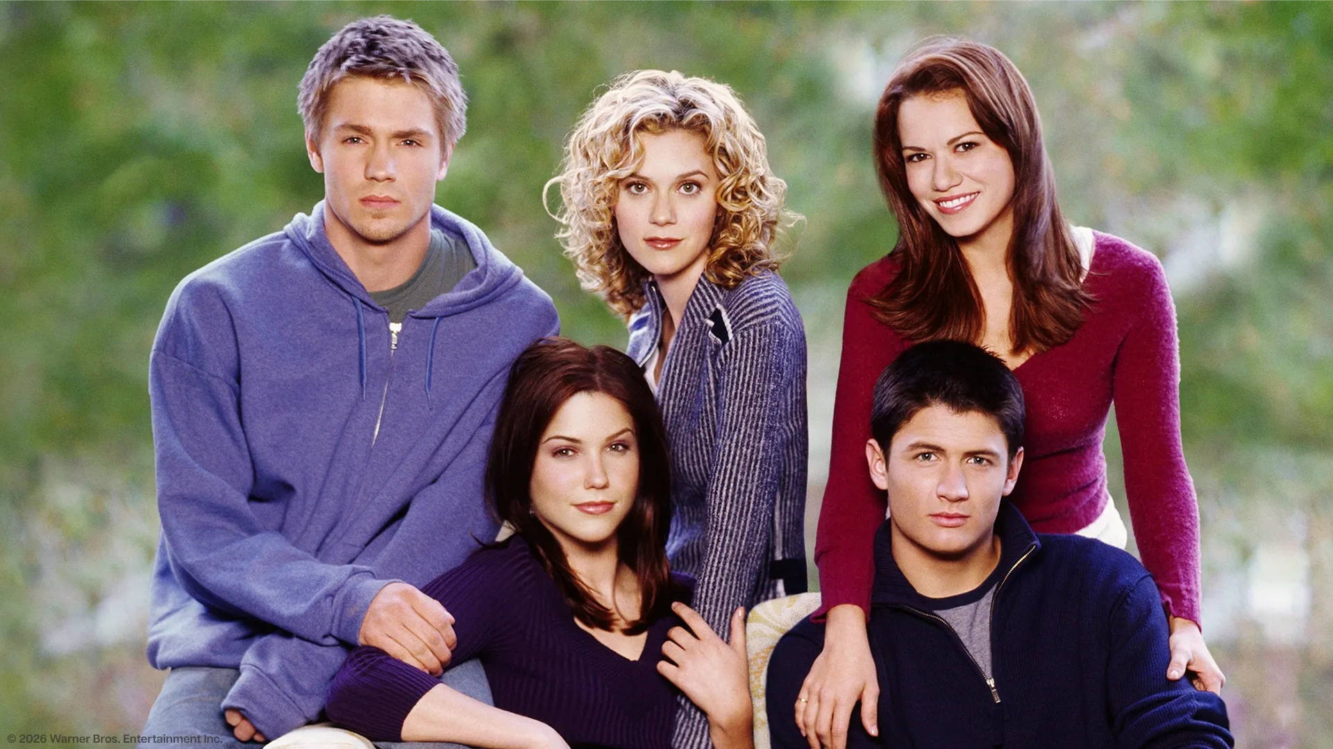 A promotional group photo of the core cast from the television series One Tree Hill posing outdoors against a blurry green background. 