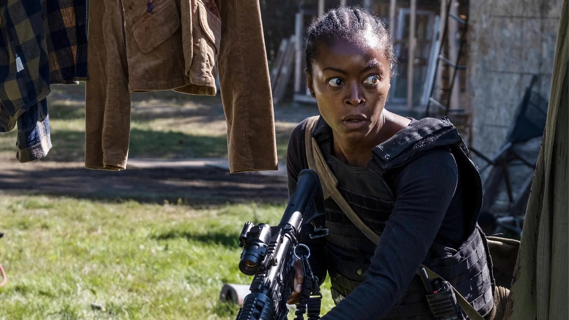 A woman in a garden, holding a gun and looking scared