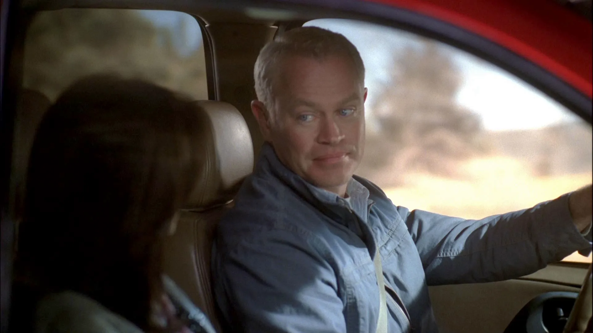 Dave Williams (Neal McDonough) drives a vehicle while casting a calculating, sideways glance toward a passenger with dark hair sitting next to him.