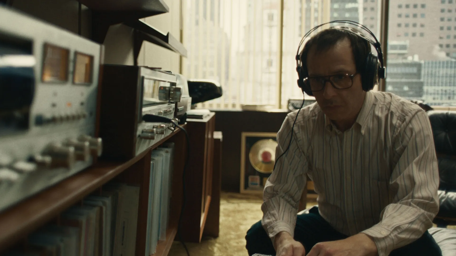 Jon Landau (Jeremy Strong), wearing headphones, listens to music on a record player.