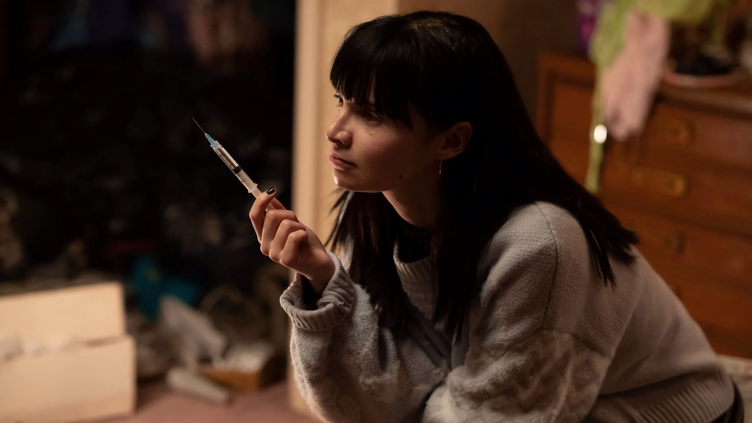 Catherine sits indoors holding a syringe.