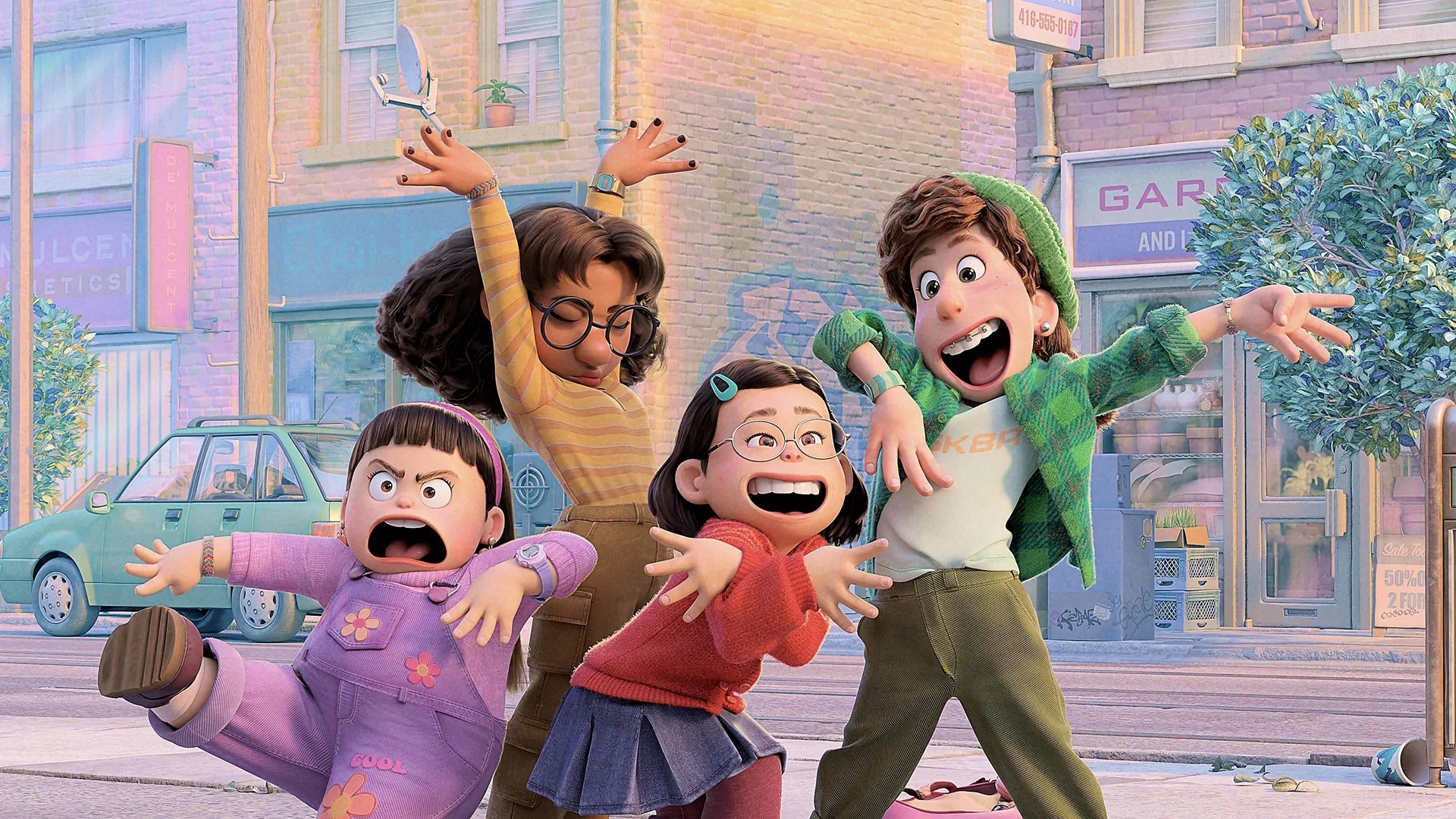 Four enthusiastic teenage girls strike dramatic, excited poses together on a city street sidewalk with colorful shopfronts and a teal car in the background, in a still from the animated movie Turning Red.