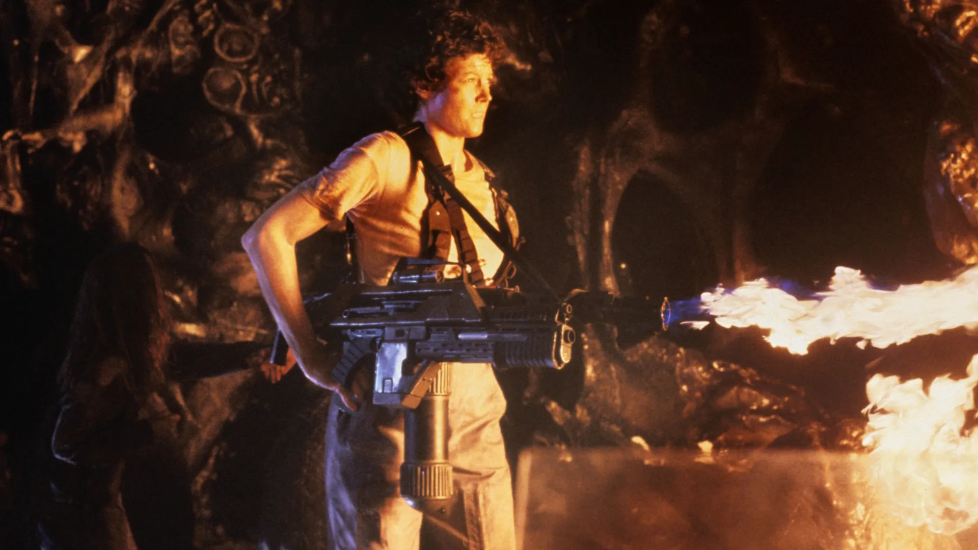 Ellen Ripley (Signourey Weaver) holding a gun in one hand and Newt, a little girl, in the other.