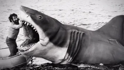 Black-and-white picture taken during production of Jaws, showing a man with his arm in the mouth of the iconic shark prop. 