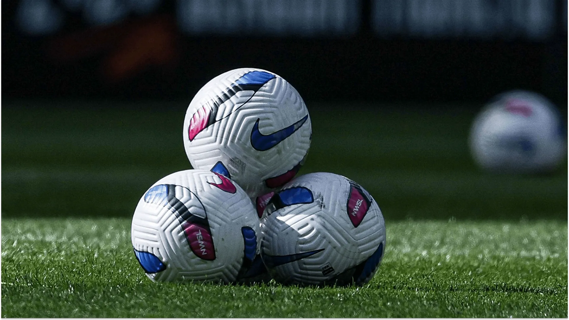 Three Nike soccer balls piled together on a grass pitch.
