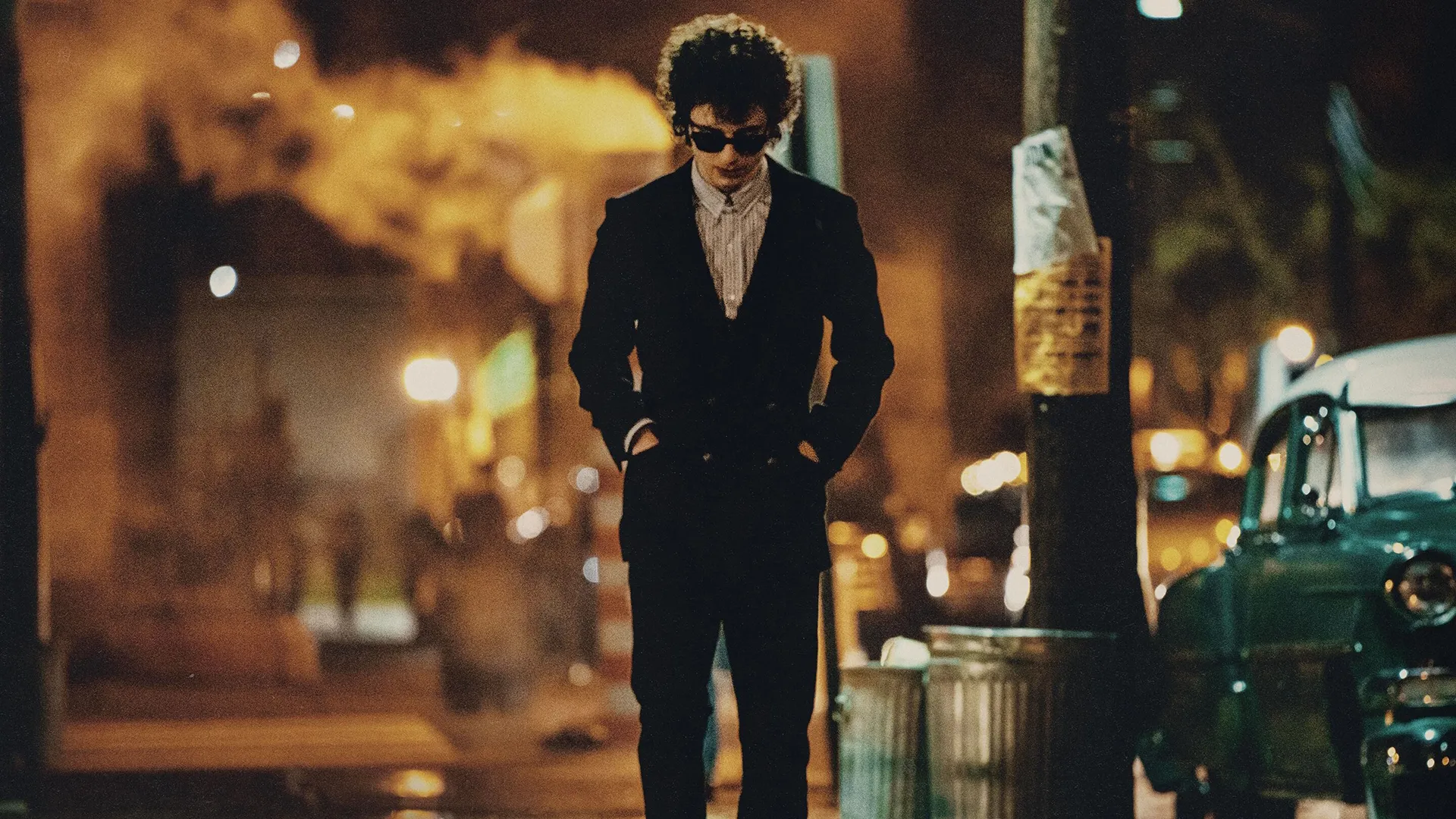 Bob Dylan (Timothy Chalamet) walking down a street with his hands in his pocket and looking at the ground.