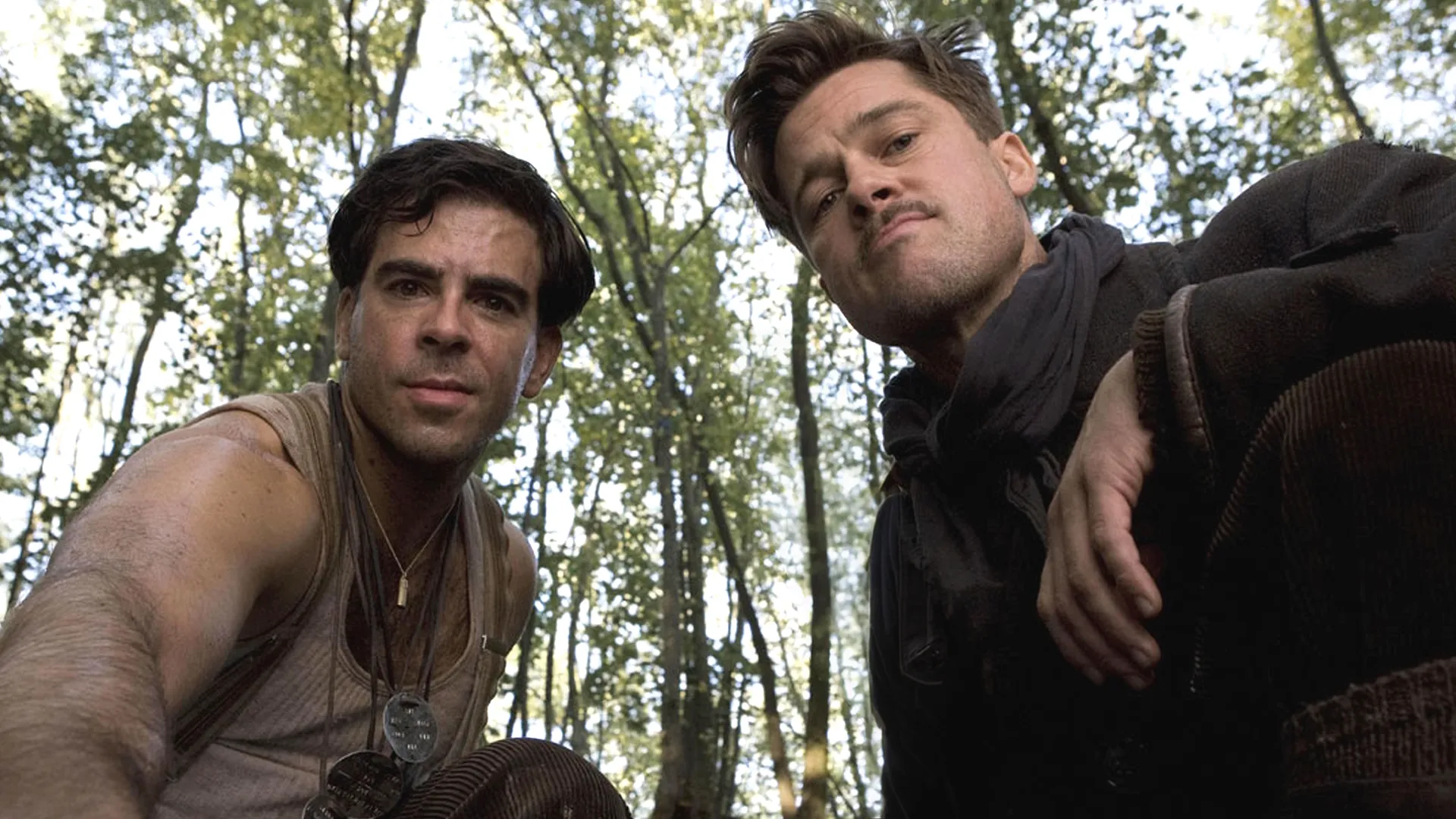A low-angle shot from the perspective of someone on the ground looking up at Eli Roth and Brad Pitt as World War II soldiers peering down in a wooded forest from the film Inglourious Basterds.