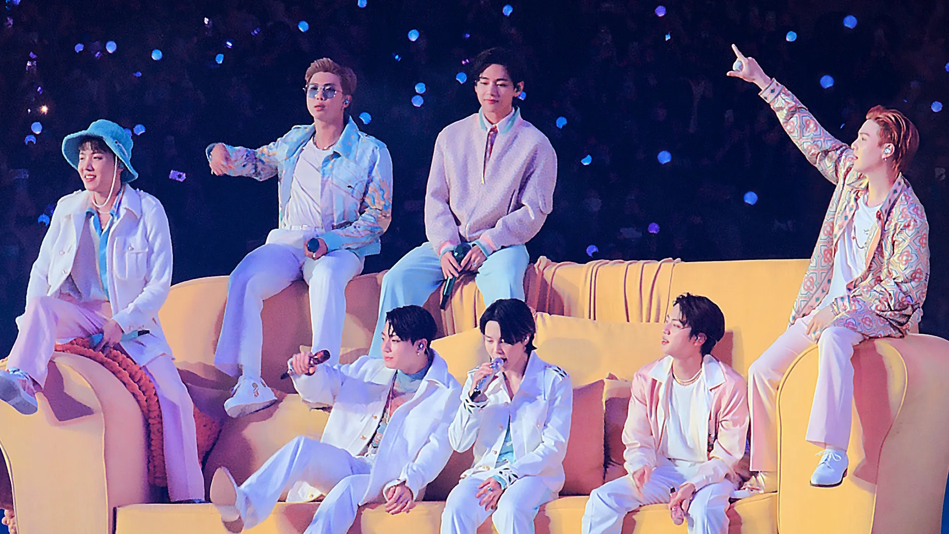 BTS band members sitting on a large yellow couch.