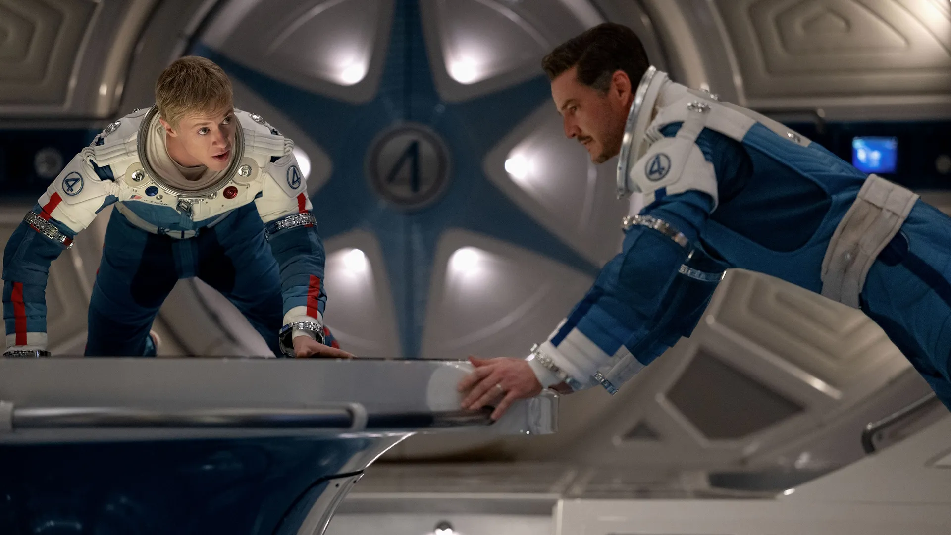 Johnny Storm and Reed Richards are wearing space suits, hovering in zero-gravity aboard a space ship
