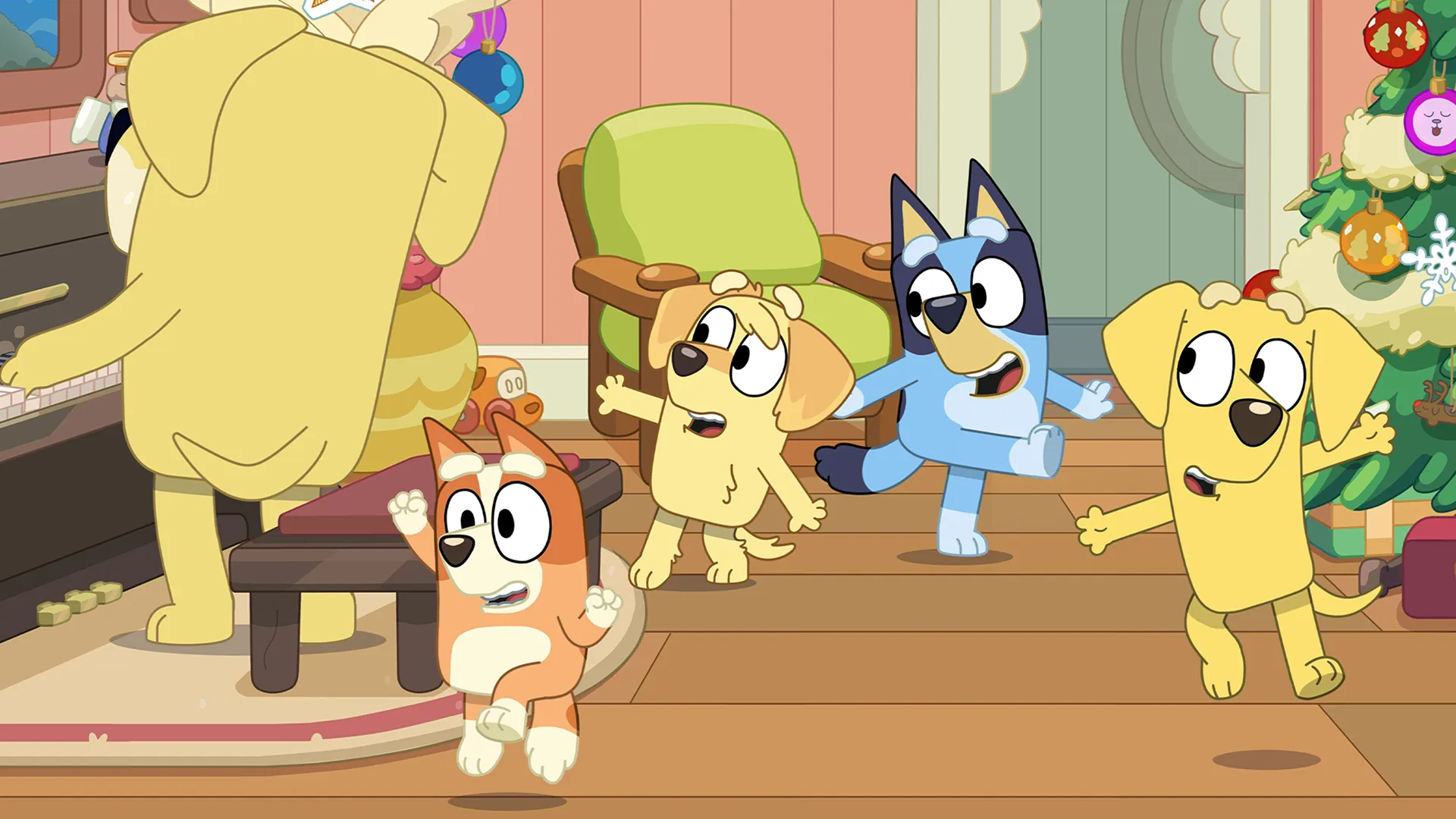 Bluey, Bingo, and their yellow Labrador friends Lucky and Chucky excitedly dance around a living room next to a decorated Christmas tree and a piano.