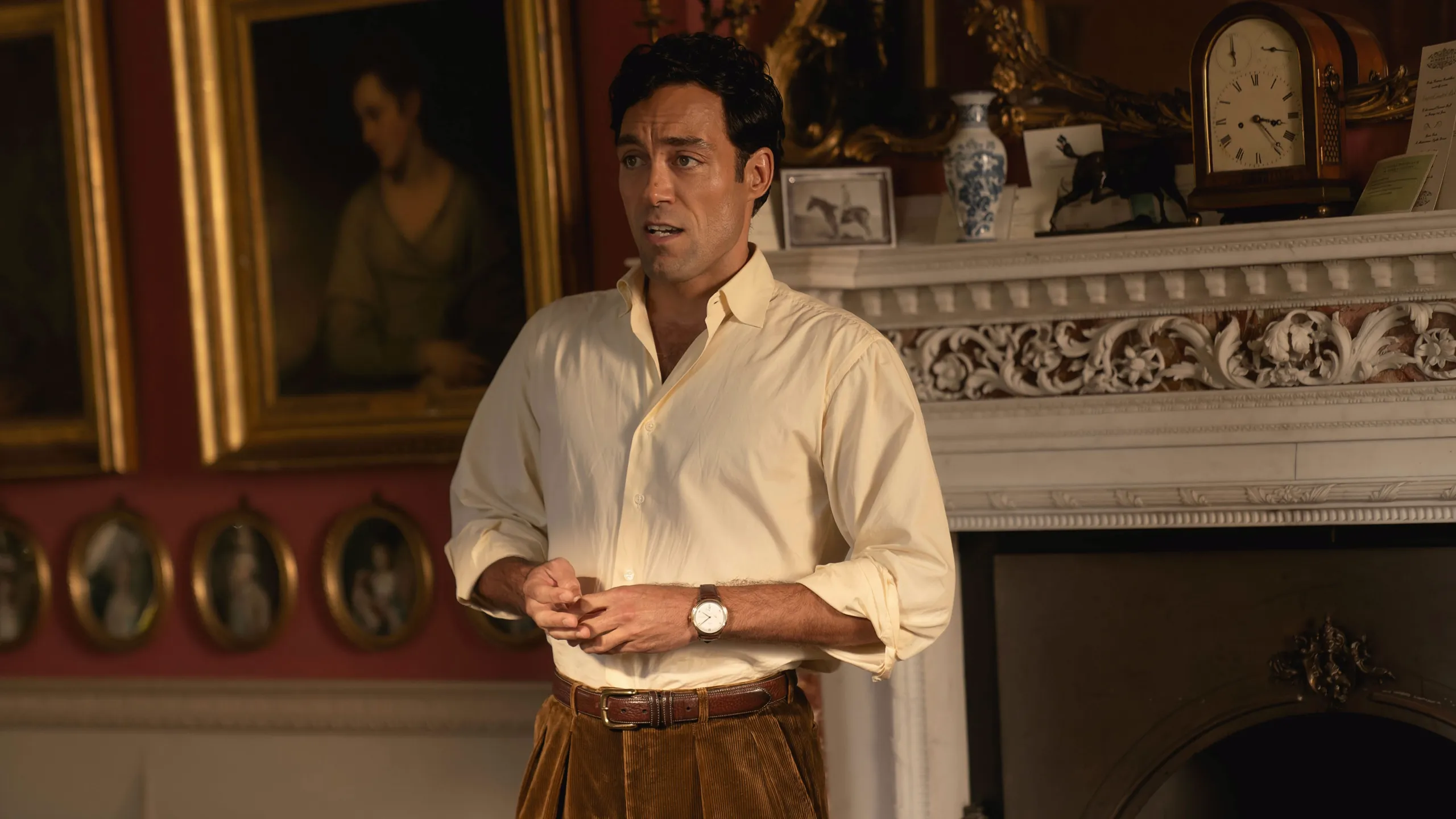 Rupert Campbell-Black (Alex Hassell) stands in a richly decorated room with a fireplace and framed portraits in Rivals.