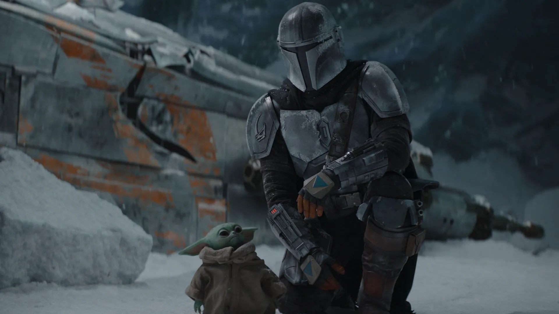 Din Djarin (Pedro Pascal) kneels down next to Grogu on a snow covered planet. Scene featured in Season 2 of The Mandalorian.