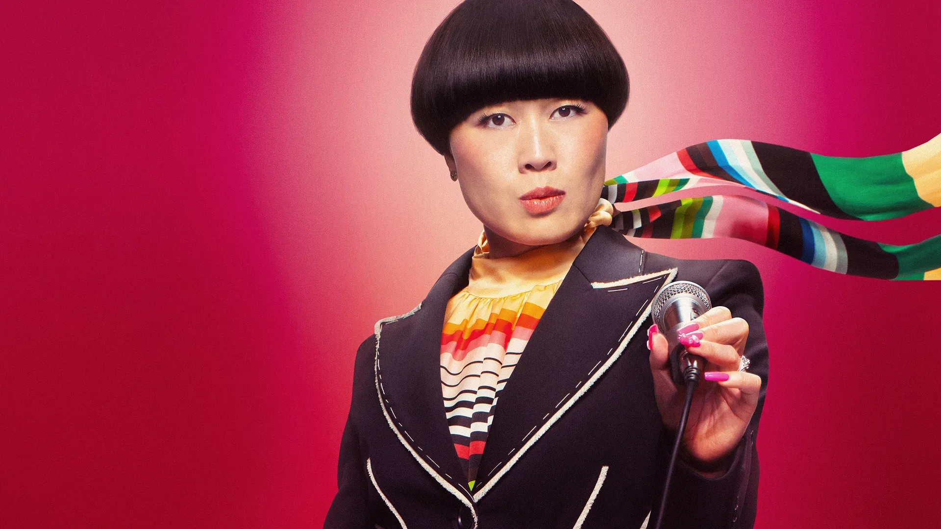 Atsuko Okatsuka looks into the camera holding a microphone in front of a red background