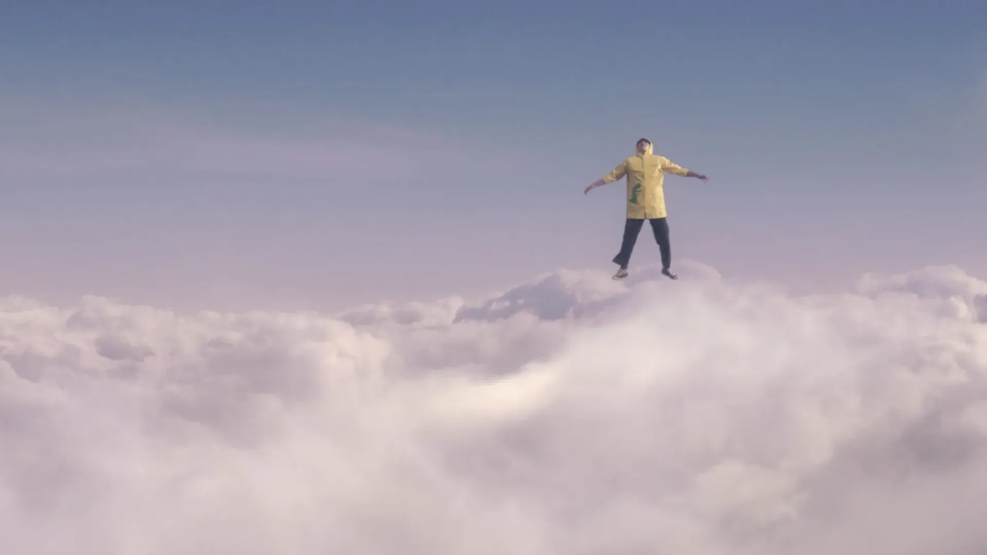 A man flying above the clouds in a yellow jacket.