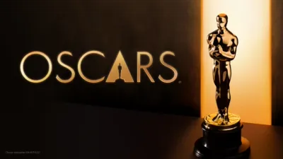 An Oscar trophy lit up by a golden light, next to the Oscars logo