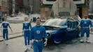 The Fantastic Four (Human Torch, Invisible Woman, Mr Fantastic and The Thing) stand next to a retro-futuristic car, looking up at something we can't see, with concerned looks on their faces