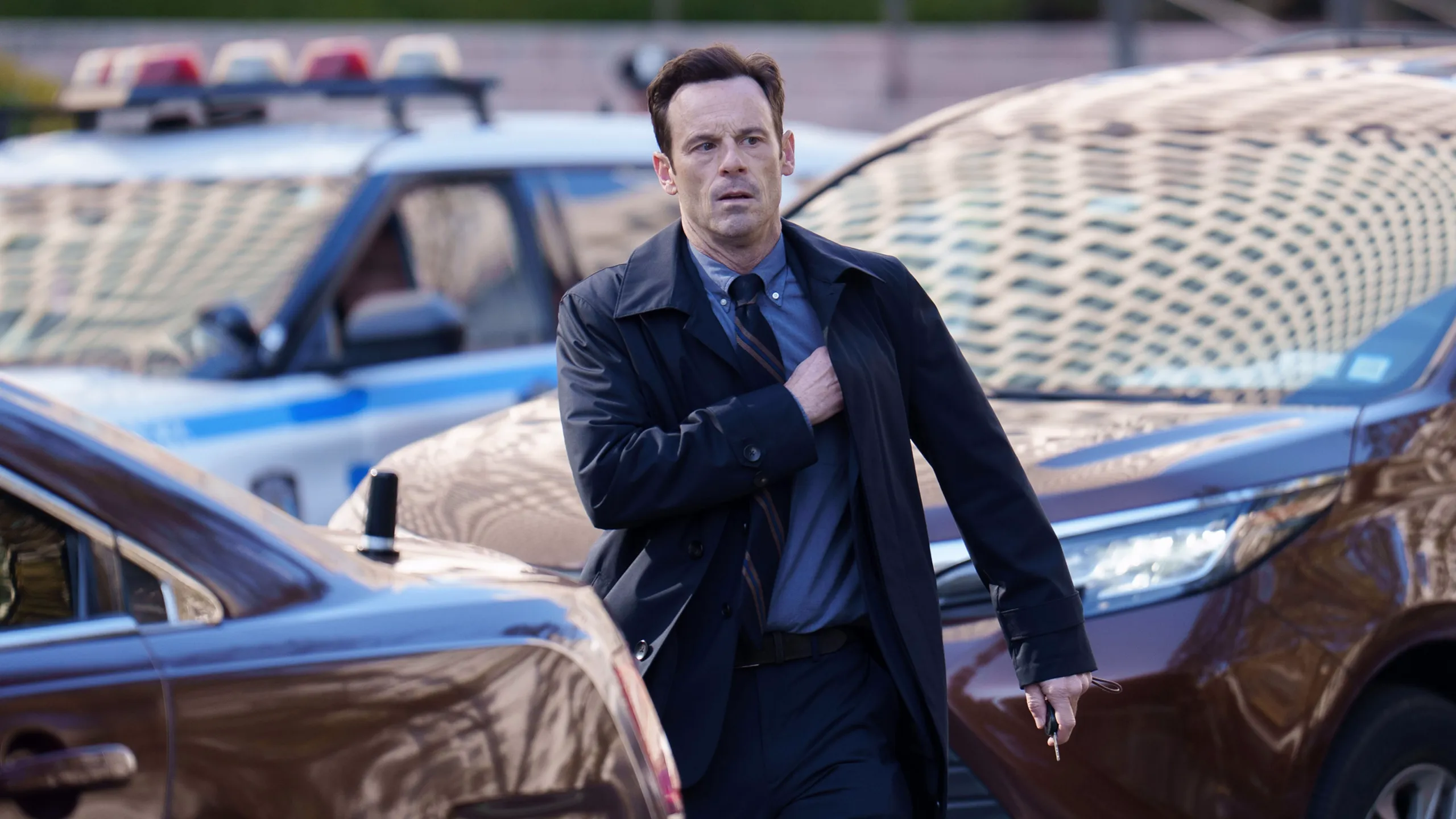 Danny walks between parked vehicles near police cars.