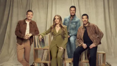 Ryan Seacrest, Carrie Underwood, Luke Bryan, and Lionel Richie pose in front of a beige background