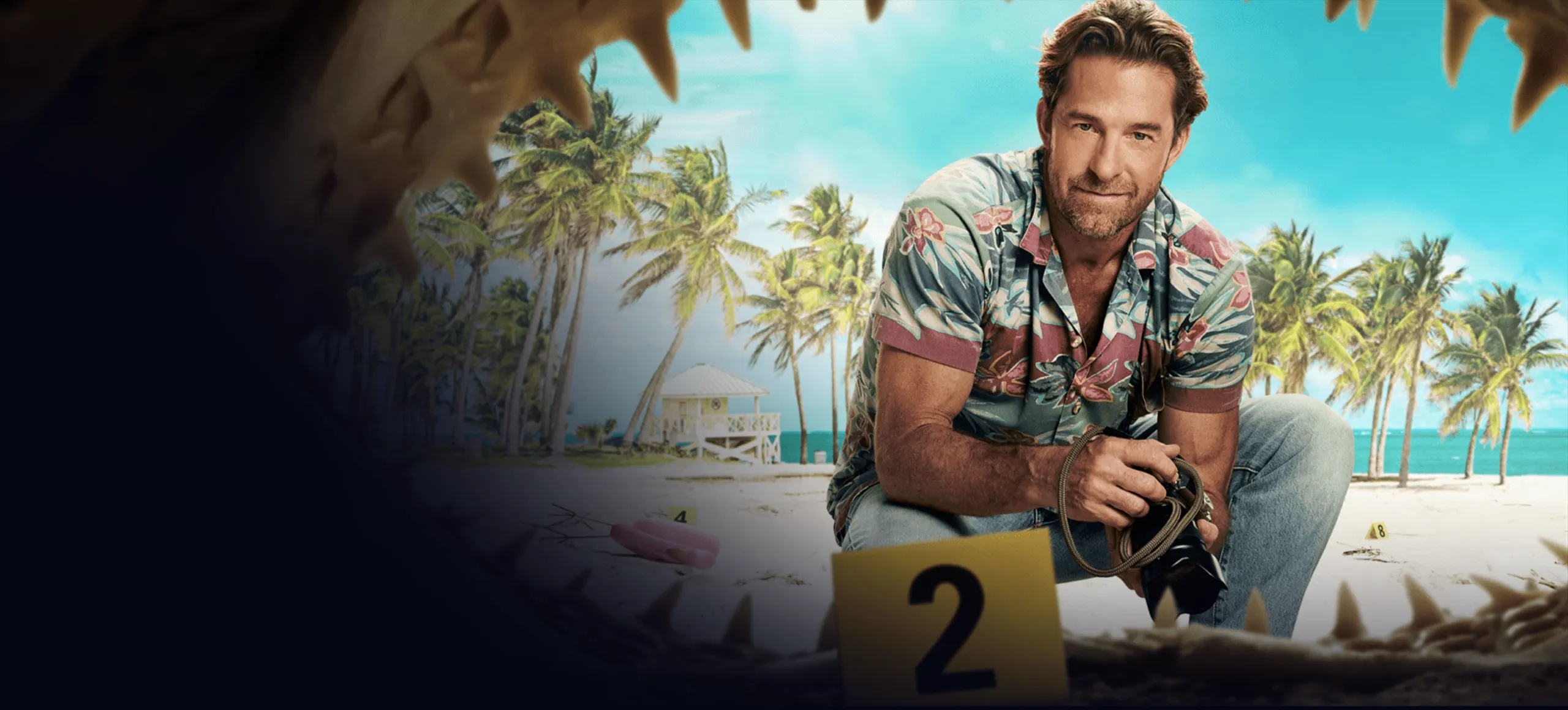 RJ in a floral shirt and jeans crouches on a tropical beach holding a camera, framed by a giant set of jaws in the foreground and a yellow evidence marker labeled "2."