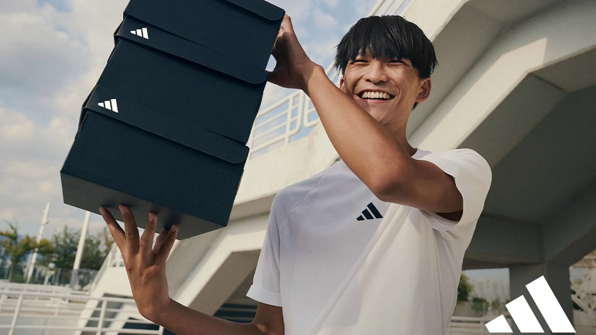 Young man holding up a few Adidas shoe boxes.
