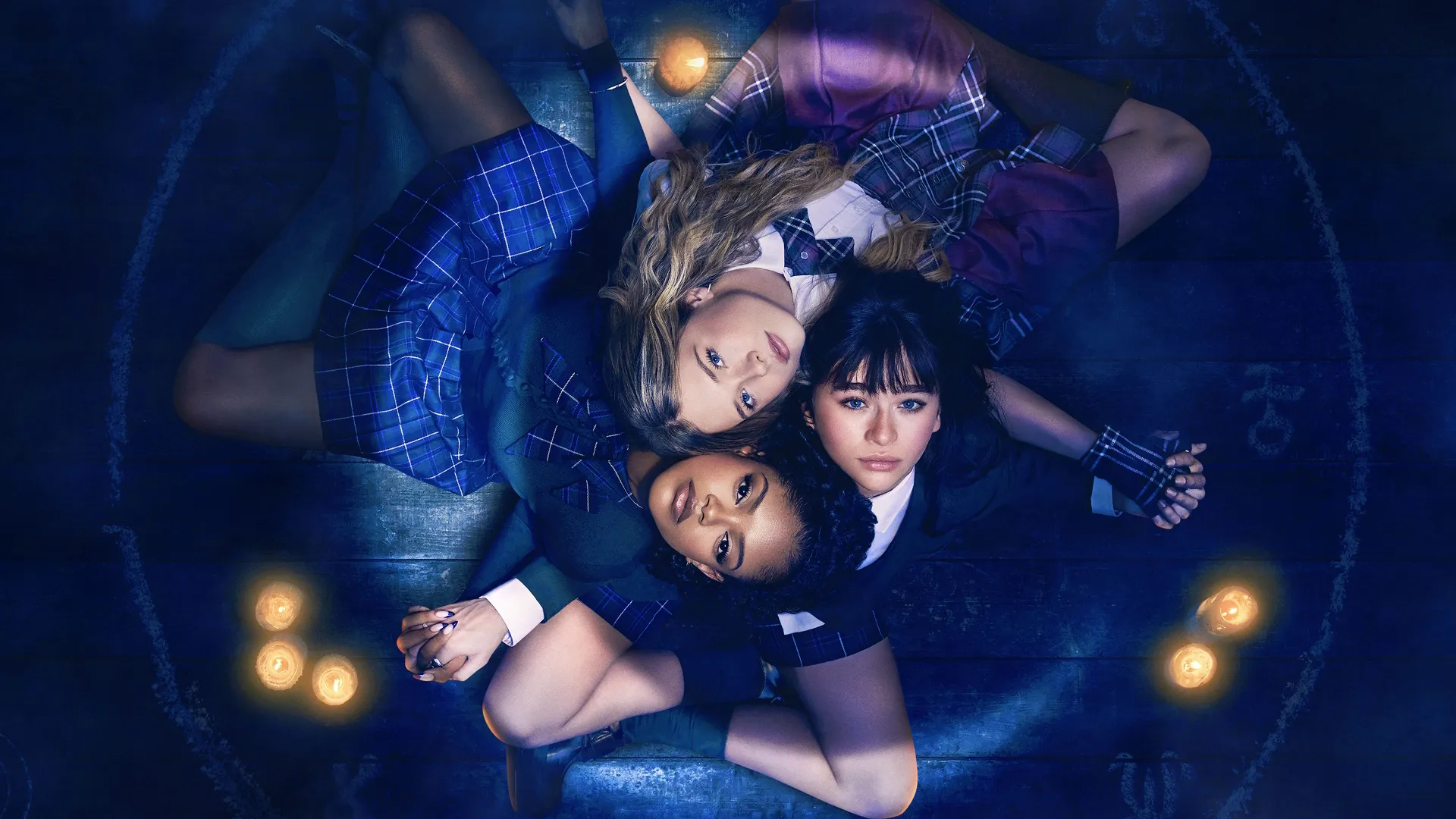 The cast of Coven Academy lying together surrounded by candles