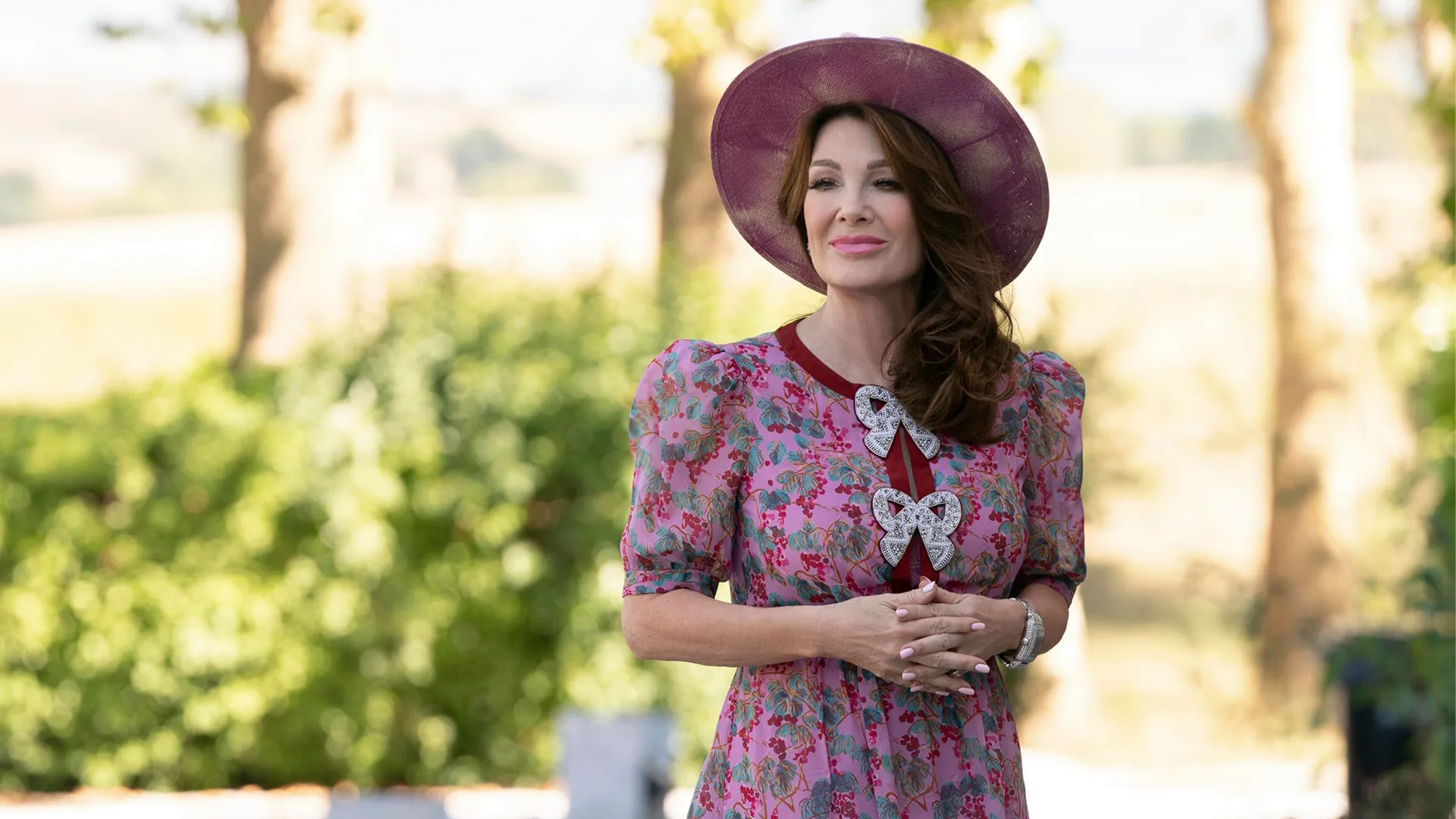Lisa Vanderpump smiles with her hands clasped in front in the sunny villa garden