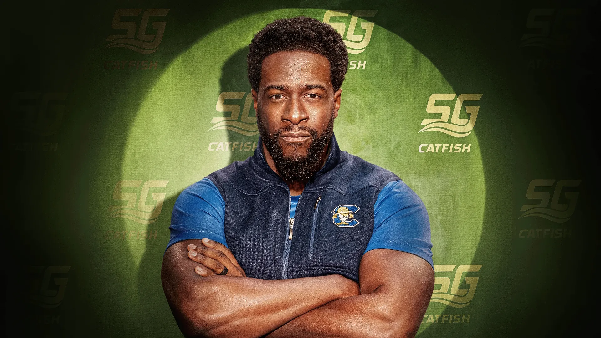 O técnico Byrd (Quentin Plair) está de pé, com os braços cruzados e uma expressão séria, contra um fundo verde texturizado coberto com o logotipo do time "SG CATFISH".