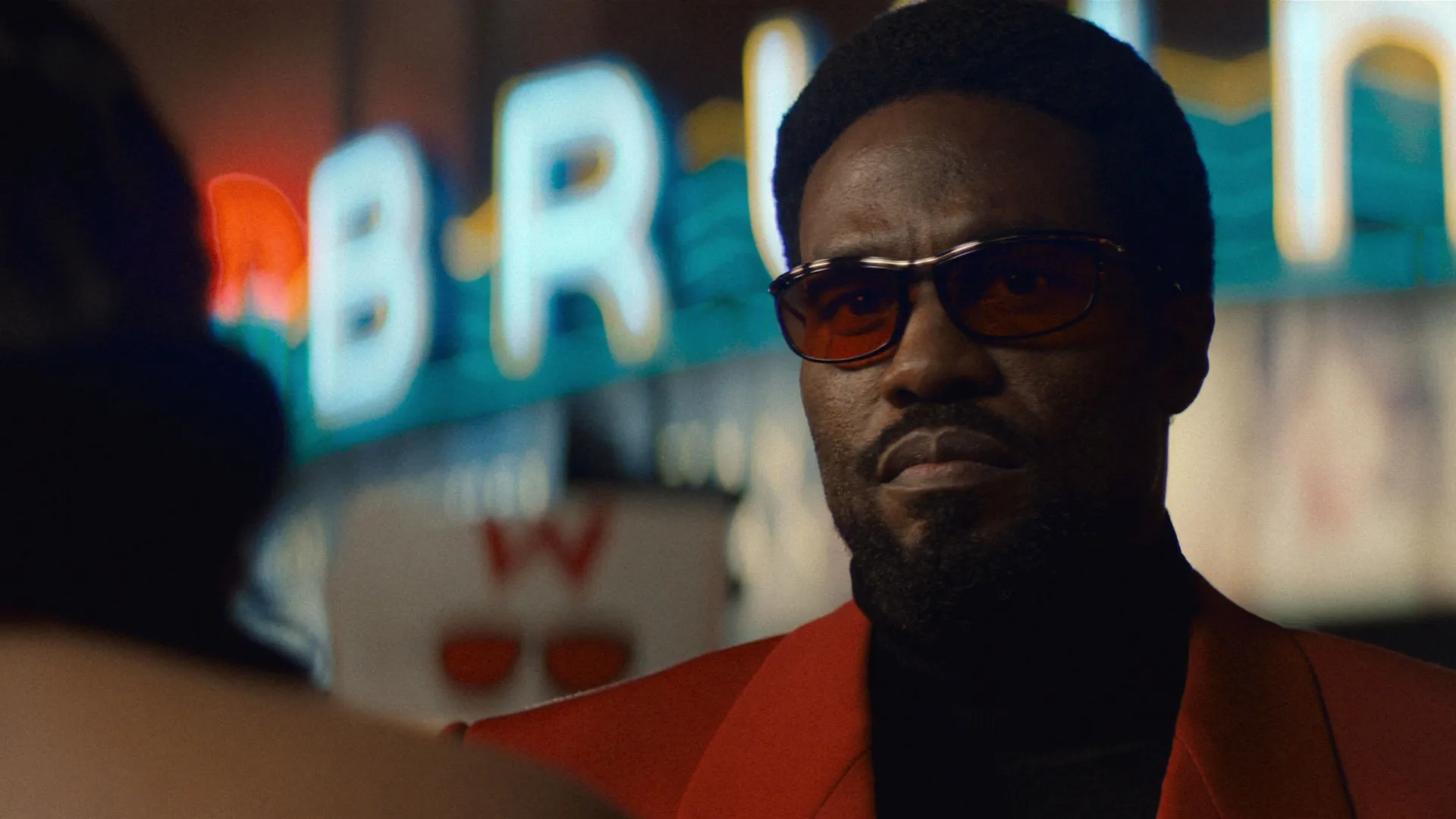 Simon Williams (Yahya Abdul-Mateen II) wearing a red suit and red-tinted glasses.