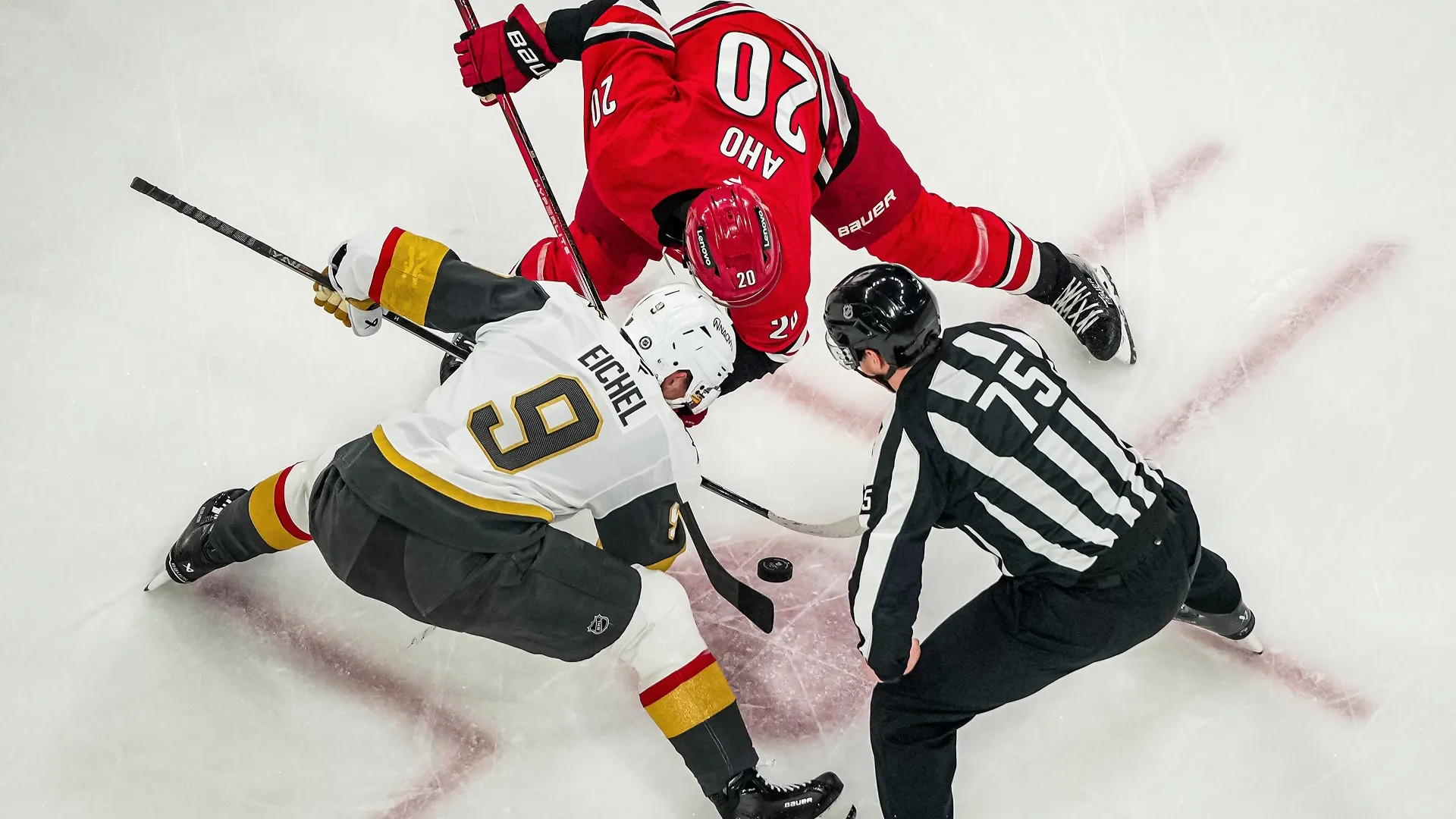 A top-down view of the referee, Jack Eichel of the Vegas Golden Knights, and Sebastian Aho of the Carolina Hurricanes during an NHL match.