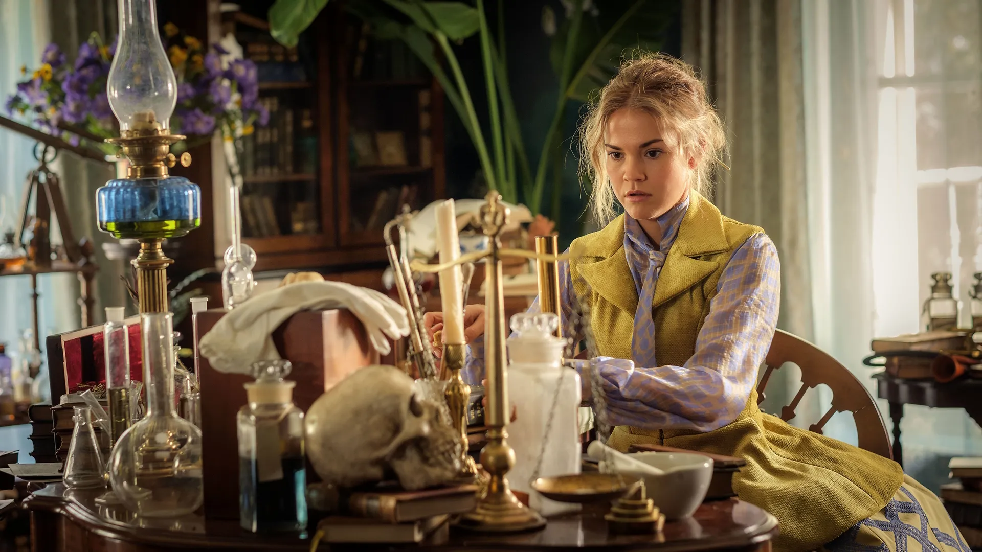 Lady Belle Fox (Maia Mitchell) sits at a table covered in Victorian curiosities