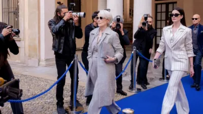 Miranda (Meryl Streep) and Andy (Anne Hathaway) walk down a blue carpet while paparazzi take photos of them in The Devil Wears Prada 2.