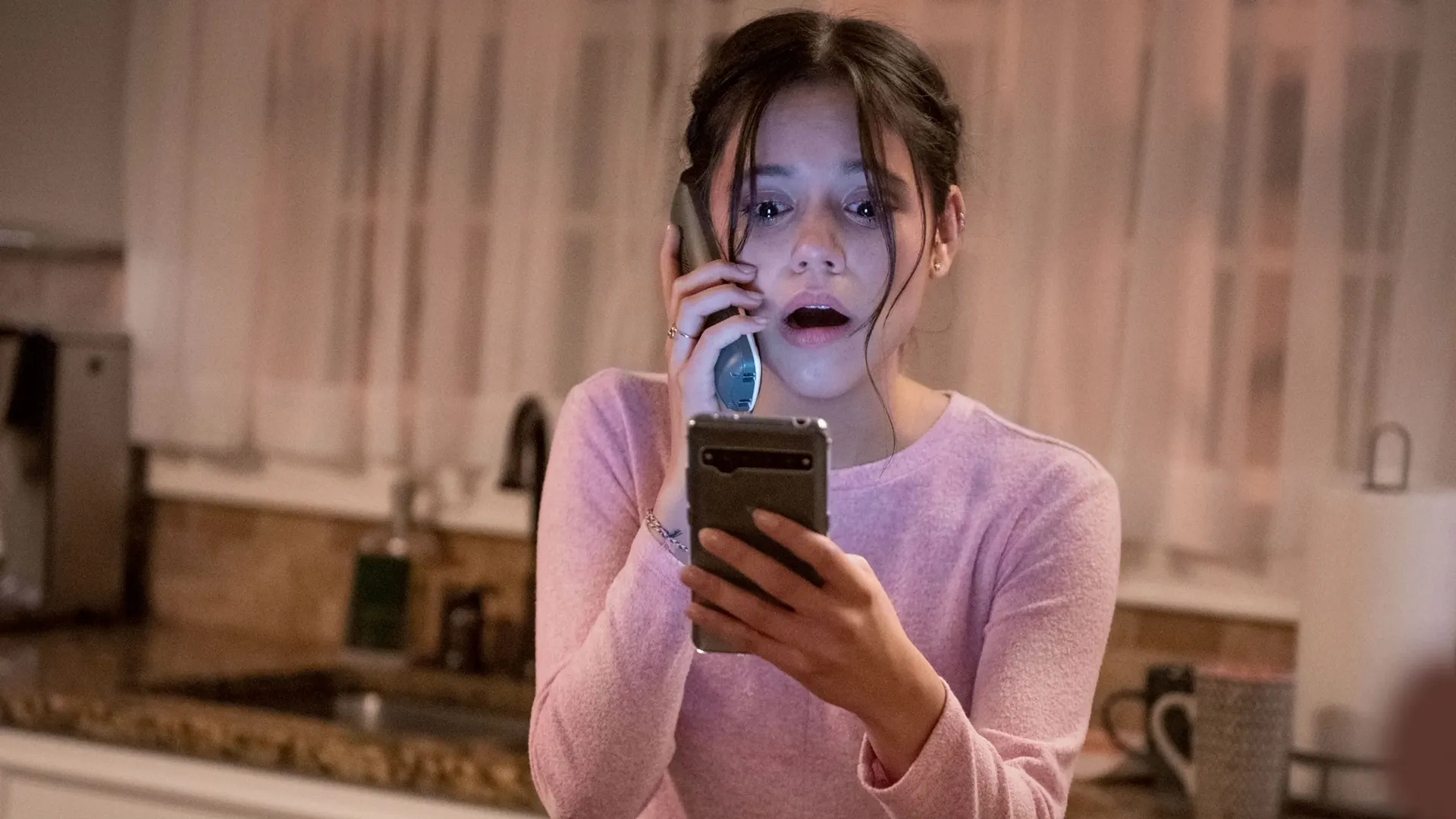 Tara Carpenter (Jenna Ortega) is looking down at a phone with a terrified and shocked expression on her face in Scream.
