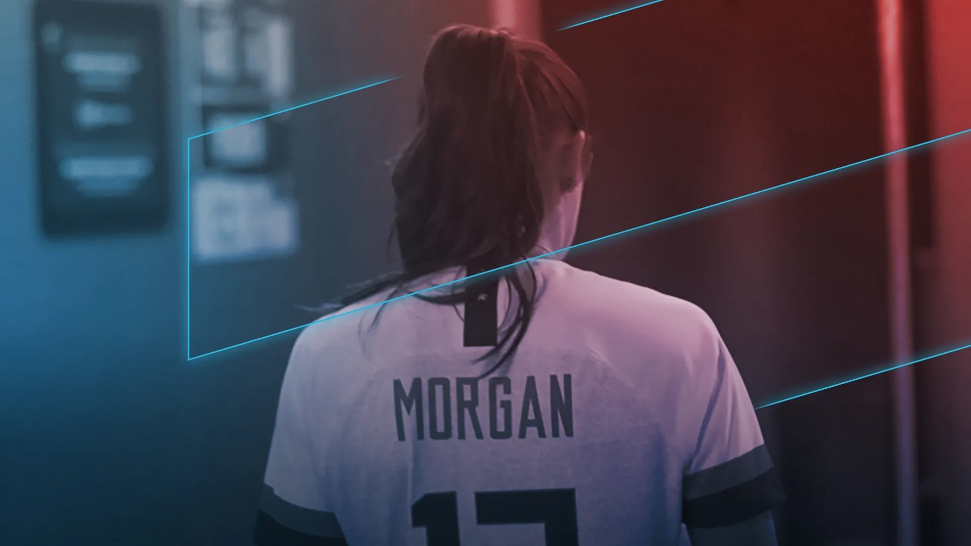 A rear view of soccer player Alex Morgan facing away from the camera in a locker room tunnel, wearing a white jersey displaying her last name above the number 13.