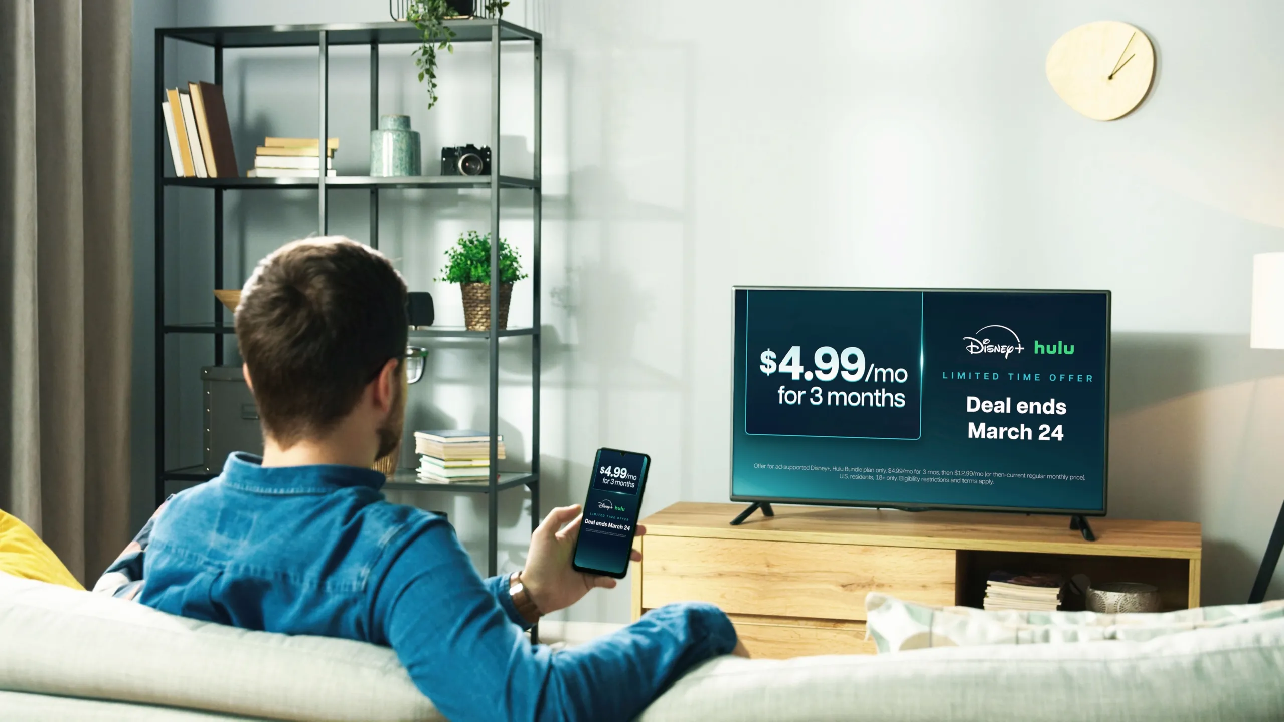 Man watching television in his living room, the TV showcases the $4.99/mo for 3 months bundle offer and available titles such as Zootopia 2 (Disney+) and Secret Lives of Mormon Wives (Hulu).