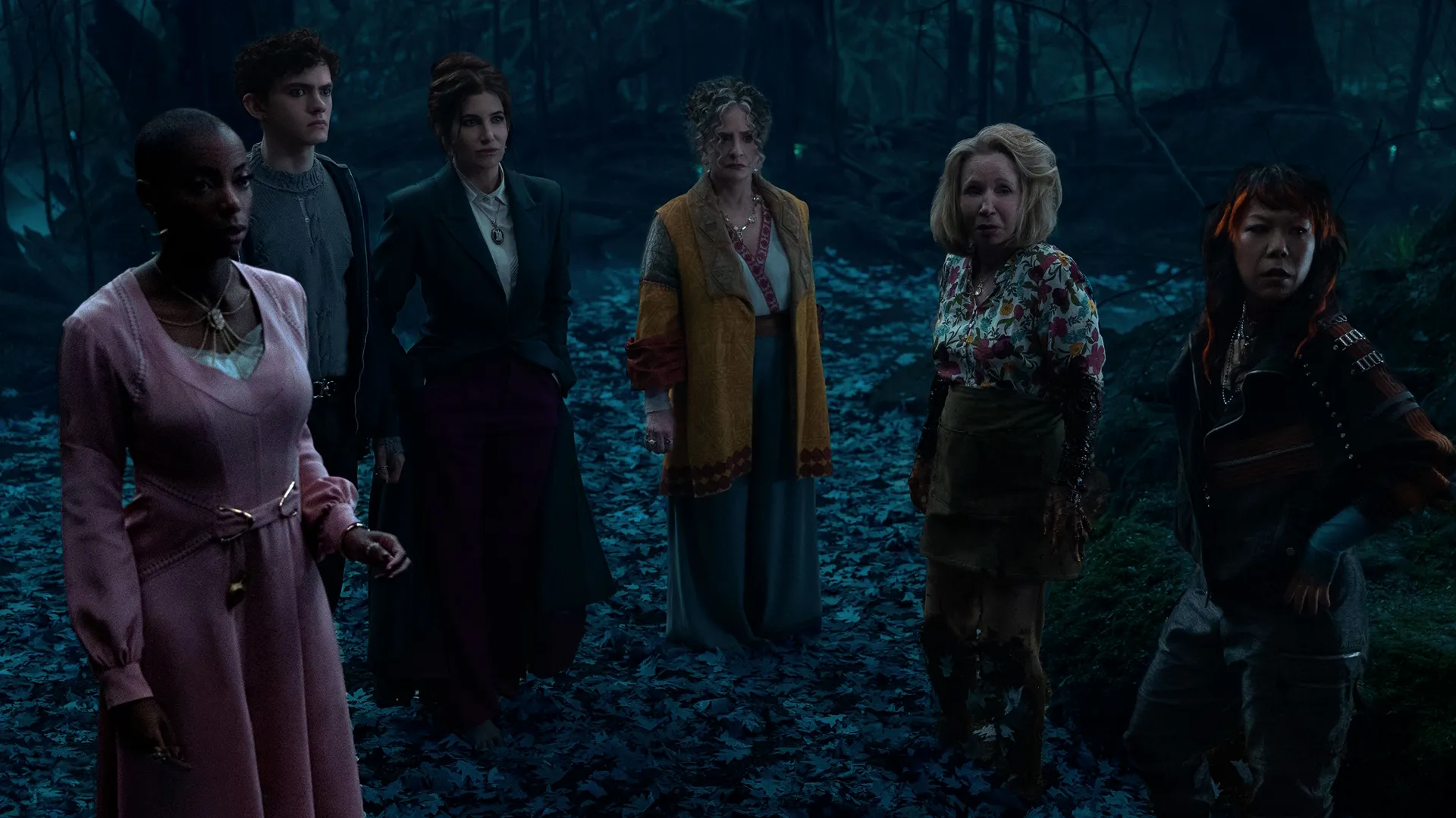 Agatha Harkness (Kathryn Hahn) and fellow characters gathered in a forest scene from Agatha All Along.