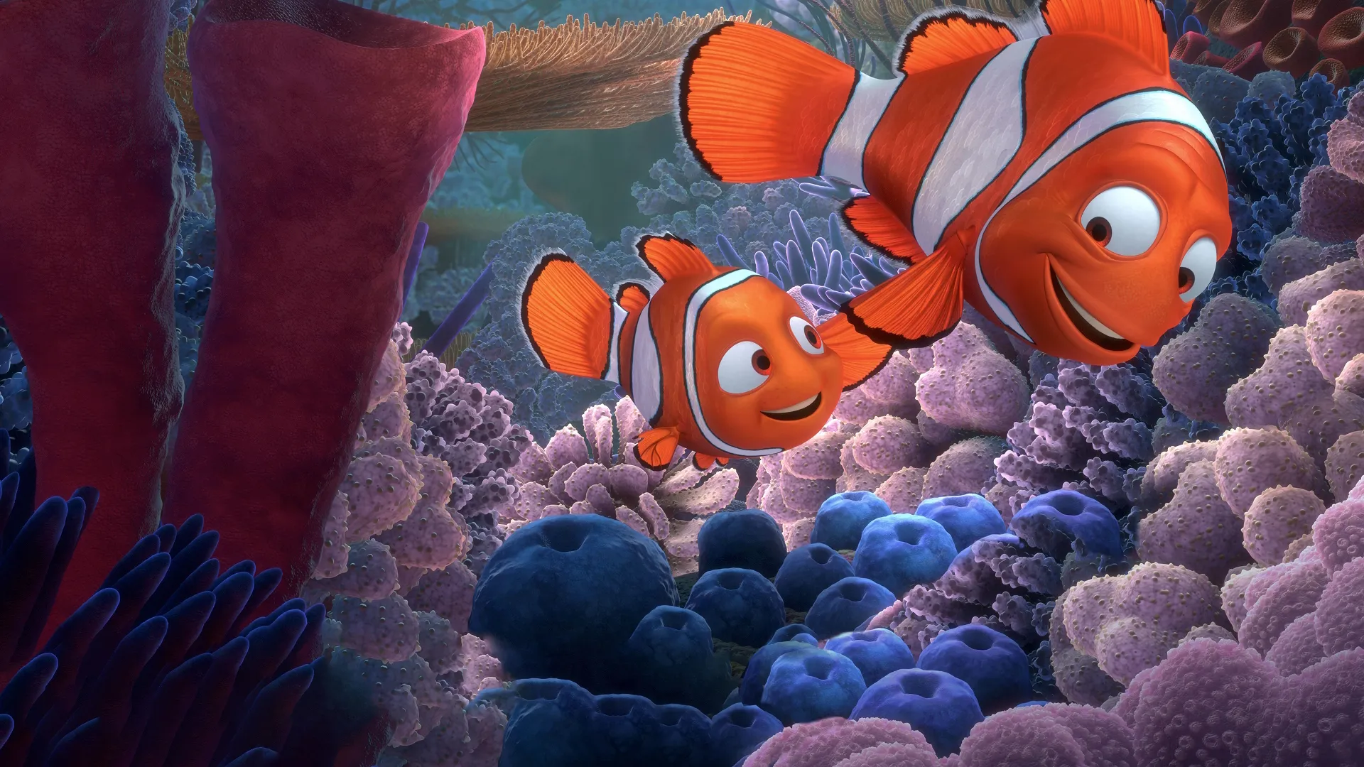 Una escena animada bajo el agua de Buscando a Nemo muestra a Nemo (Alexander Gould) nadando feliz junto a su padre, Marlín (Albert Brooks), en medio de un vibrante arrecife de coral lleno de anémonas violetas, azules y naranjas