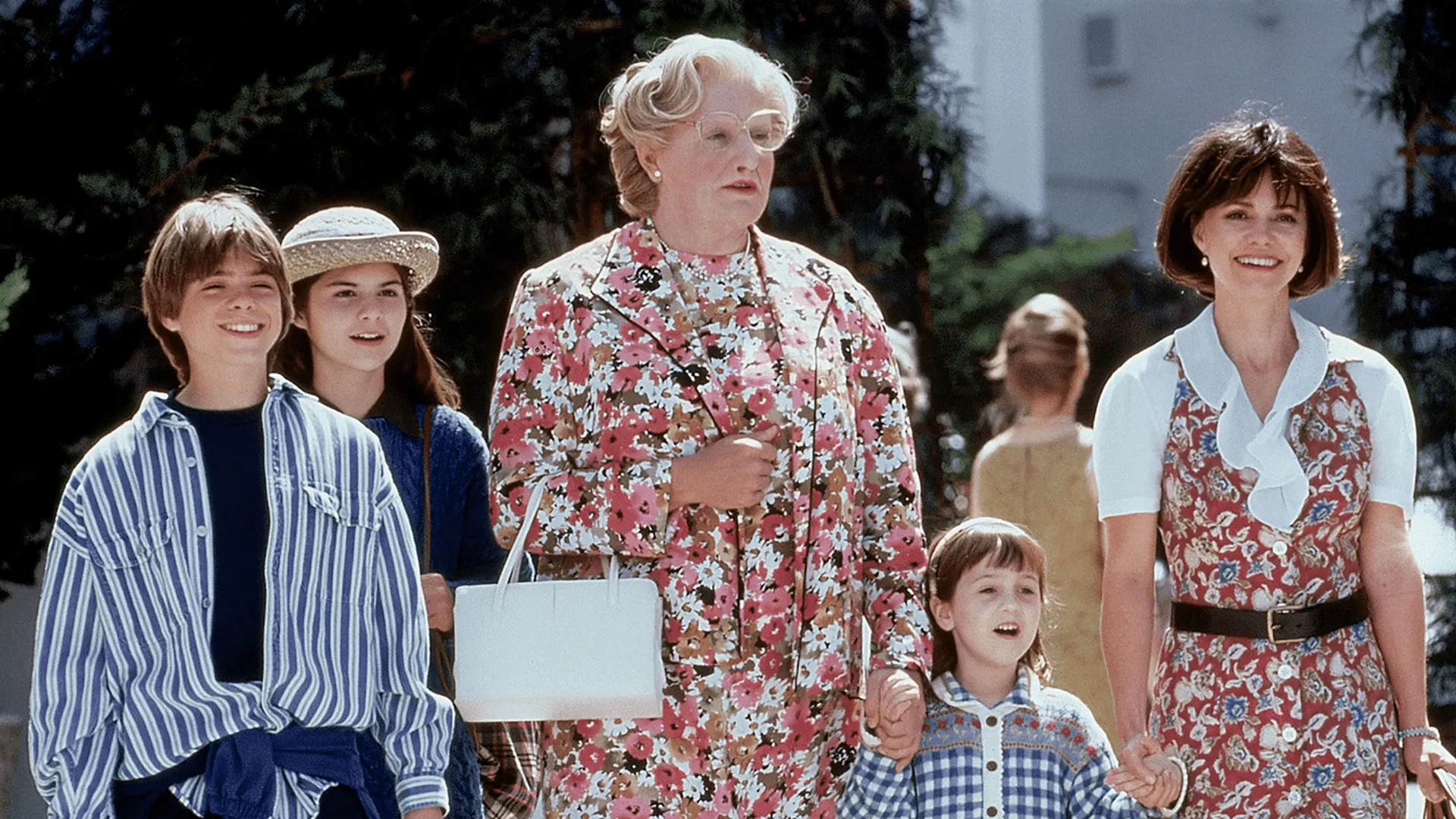 Robin Williams as Mrs. Doubtfire walking outdoors with Sally Field as Miranda Hillard and the kids, played by Lisa Jakub, Matthew Lawrence, and Mara Wilson, in a scene from the 1993 comedy movie Mrs. Doubtfire.