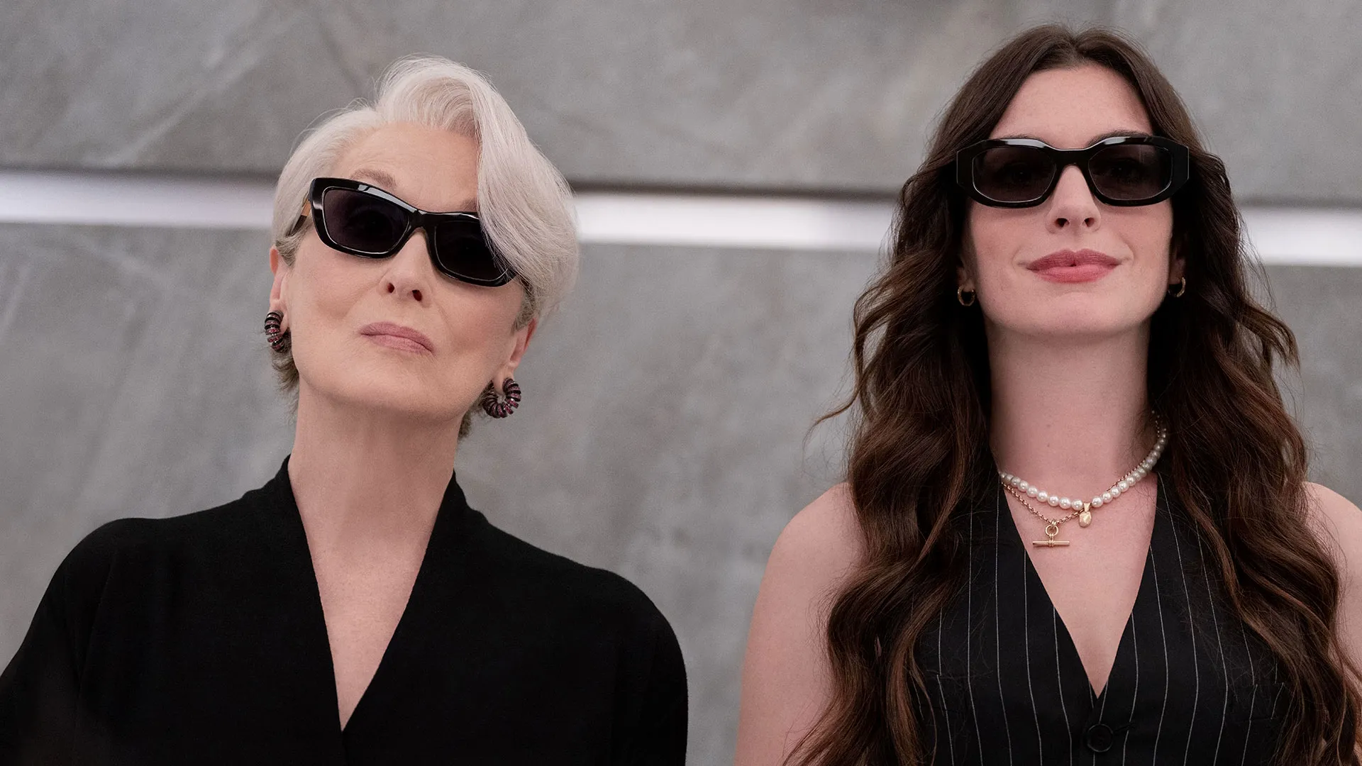 Key art for The Devil Wears Prada 2 featuring Miranda Priestly and Andy Sachs fashionably dressed wearing dark sunglasses against a minimalist grey backdrop.