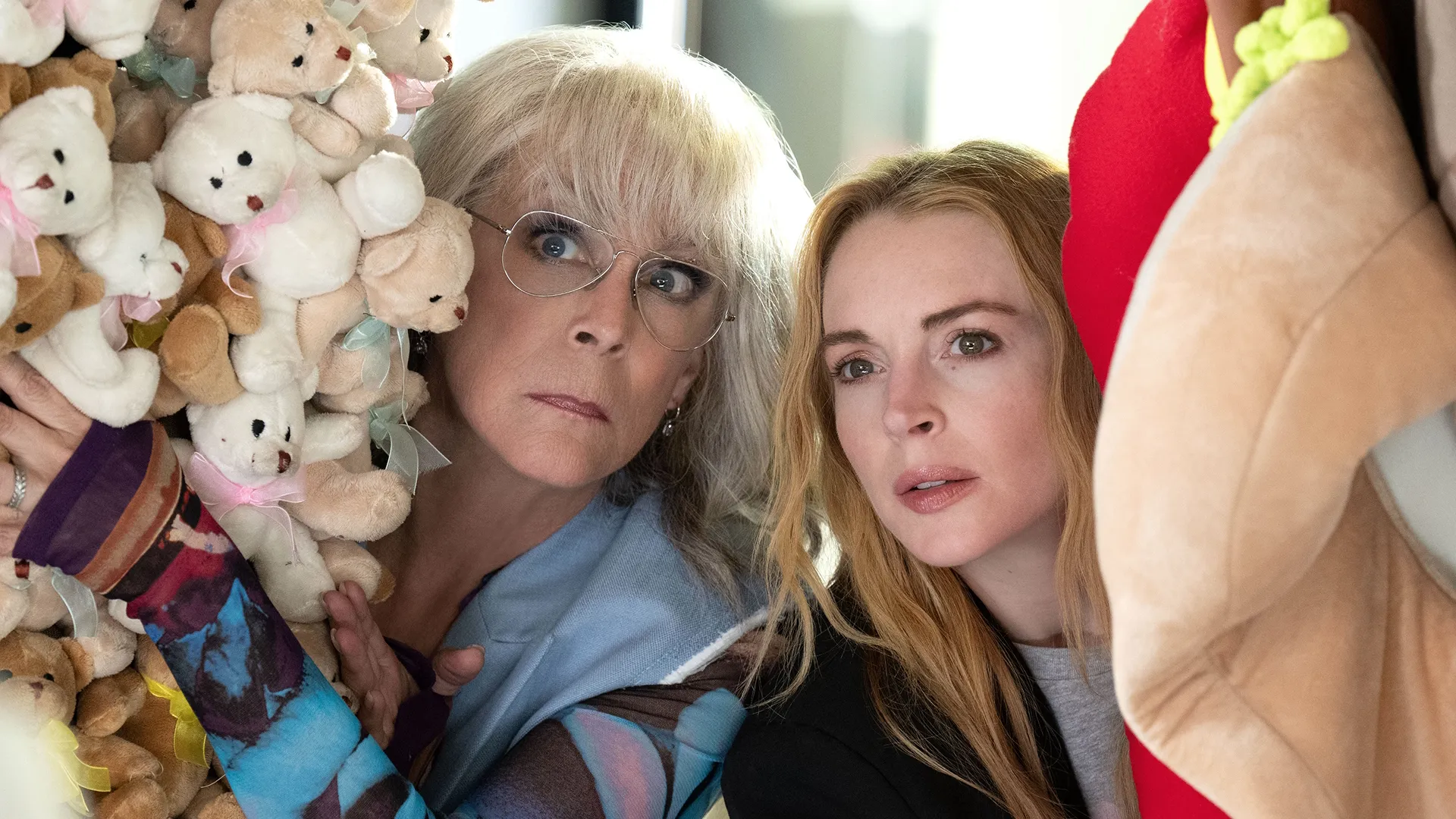 Tess Coleman (Jamie Lee Curtis) and Anna Coleman (Lindsay Lohan) hide behind stuffed toys.