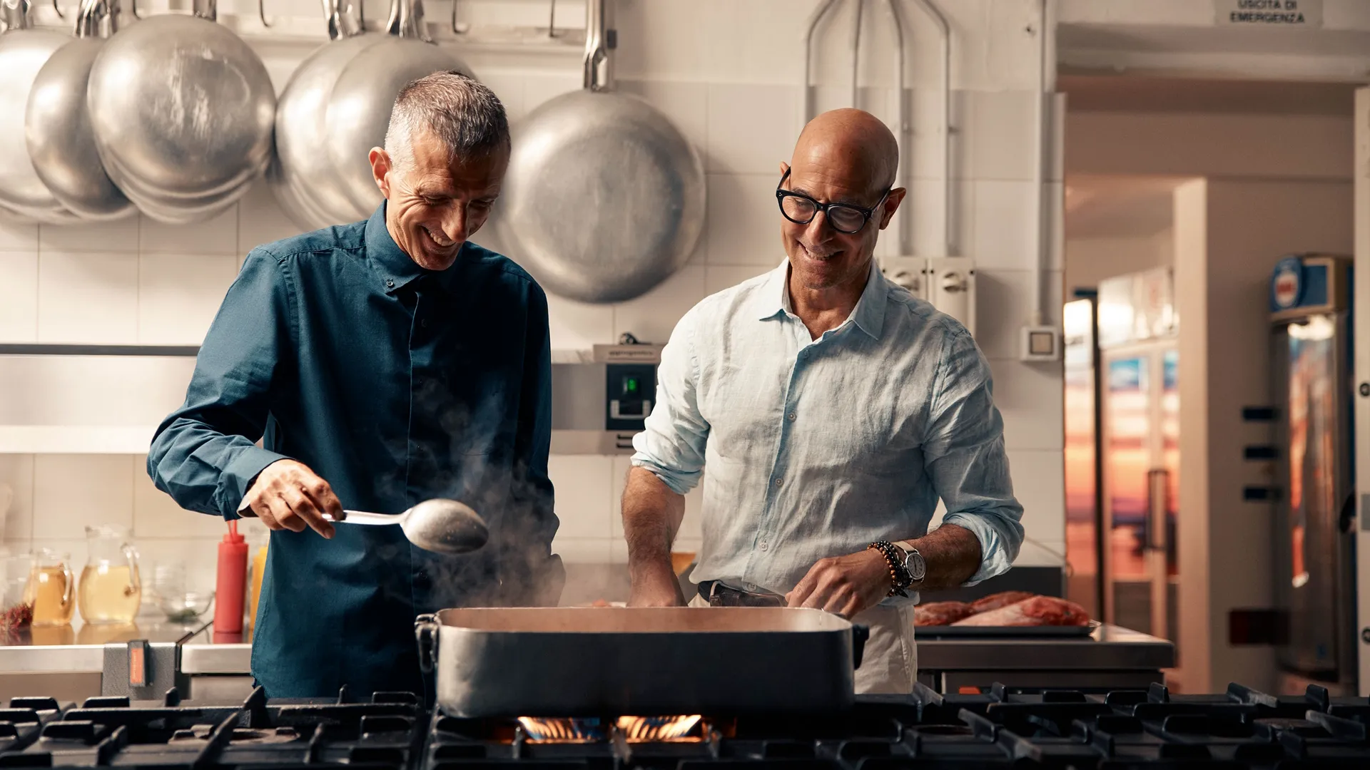 Stanley Tucci and a chef smile as they cook