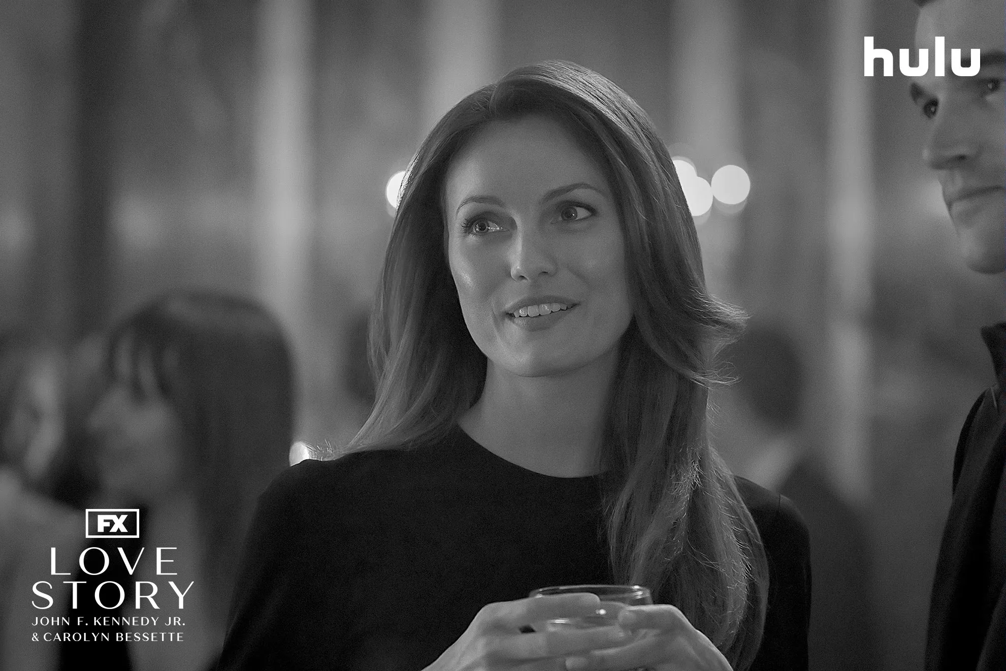 Carloyn Bessette (Sarah Pidgeon) at an event in a black and white set photo from FX's Love Story.