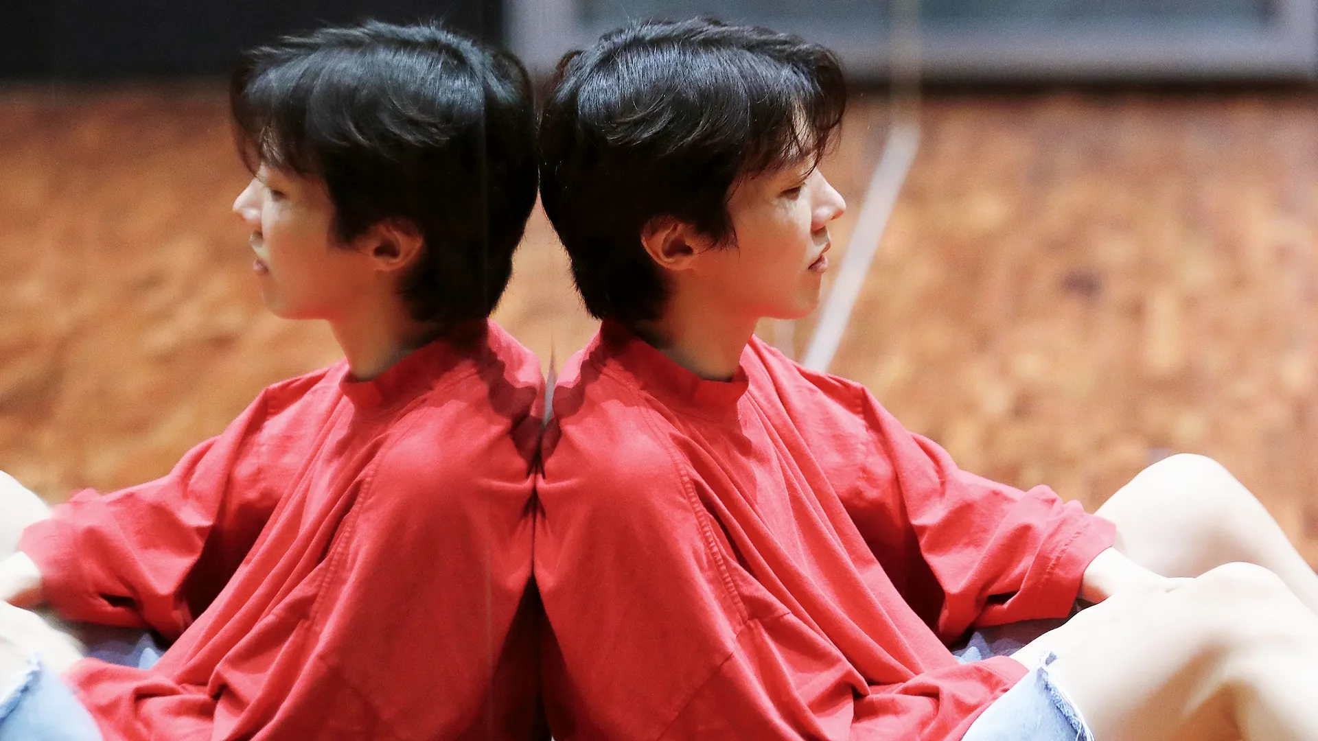 Artist j-hope sits with his back against a mirror in a dance studio.