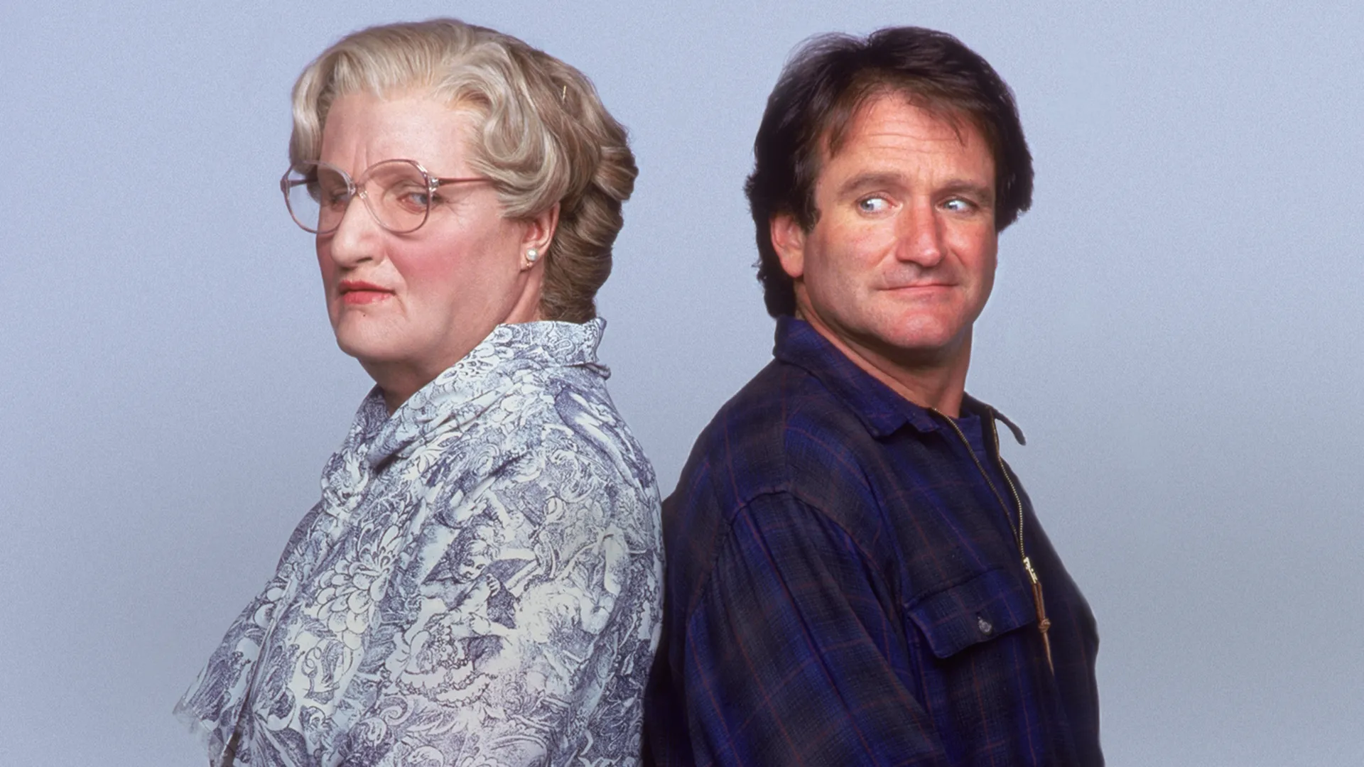 Una clásica imagen promocional de Papá por siempre muestra a Daniel Hillard (Robin Williams) de pie, espalda con espalda con su alter ego, la Sra. Doubtfire (Robin Williams); Daniel mira por encima de su hombro con una sonrisa a la Sra. Doubtfire, que mira de lado y tiene una blusa estampada y anteojos sobre un fondo gris