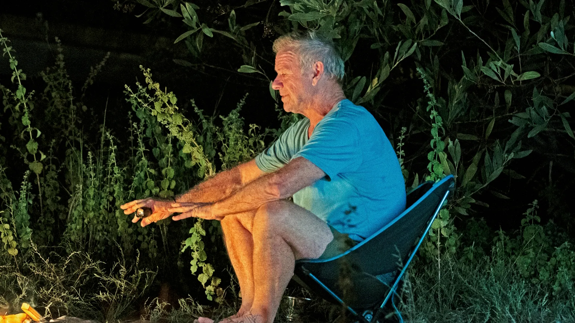 Craig Hemsworth sitting in a folding camp chair next to a fire at night,