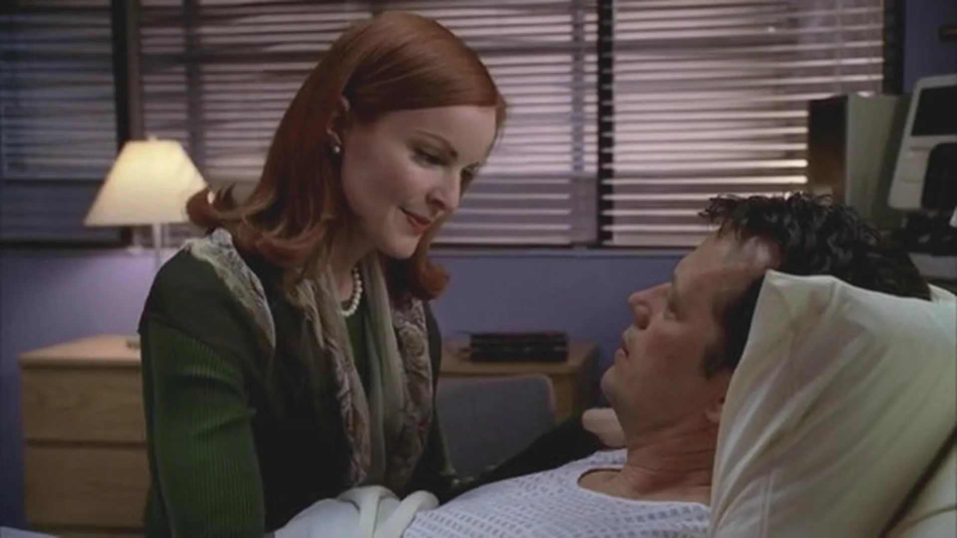 Bree Van de Kamp (Marcia Cross) looks down with a calm, gentle smile at her husband, Rex Van de Kamp (Steven Culp), who lies in a hospital bed looking back up at her.
