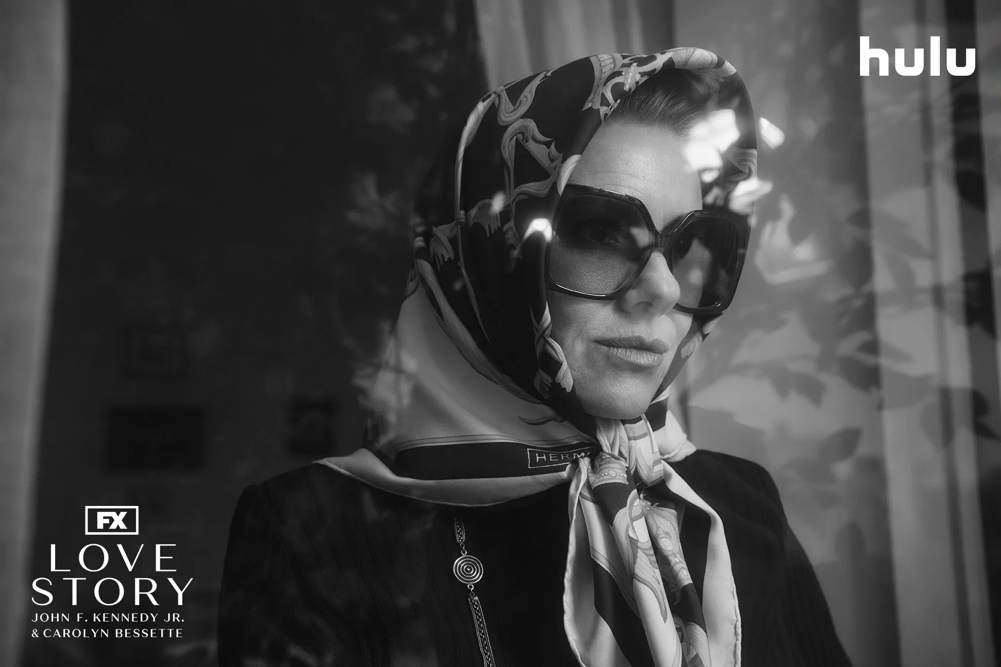 Jackie Kennedy Onassis (Naomi Watts) wearing large glasses and head covering in a black and white set photo from FX's Love Story.