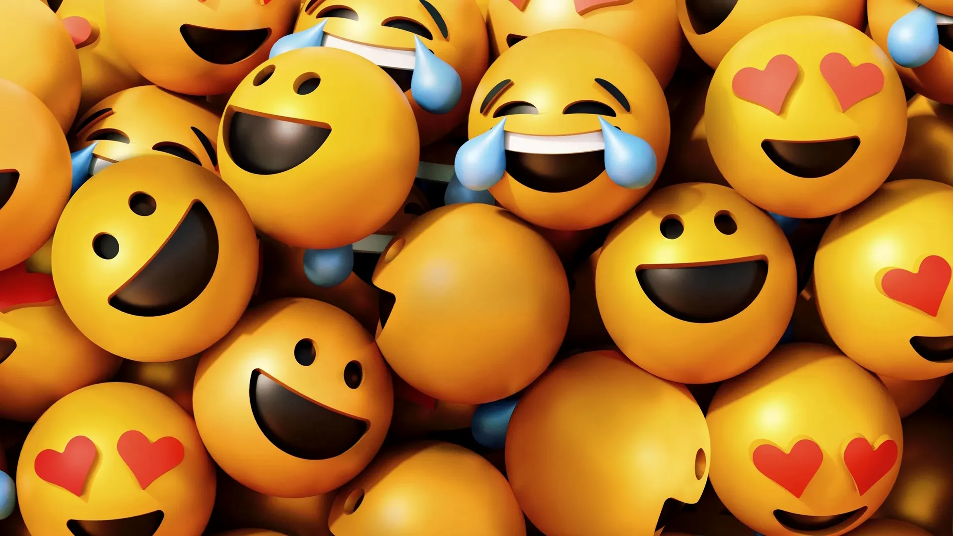A large bundle of spherical yellow balls featuring common emoji icons such as the crying laughing emoji, wide smile, and loveheart eyes.