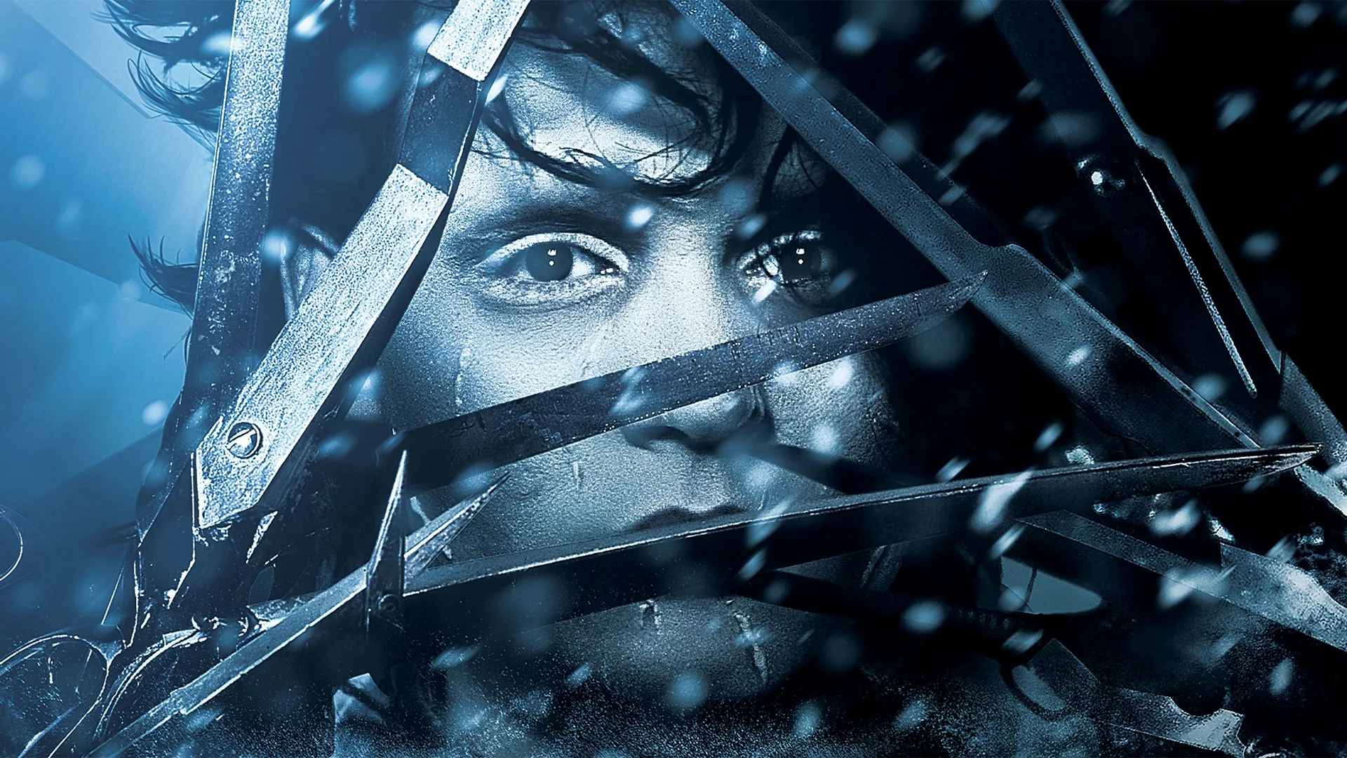 A close-up movie still from Edward Scissorhands shows Johnny Depp's pale, scarred face peering through a dense, crisscrossed web of sharp scissor blades as white snow falls around him in a cool blue-toned light.